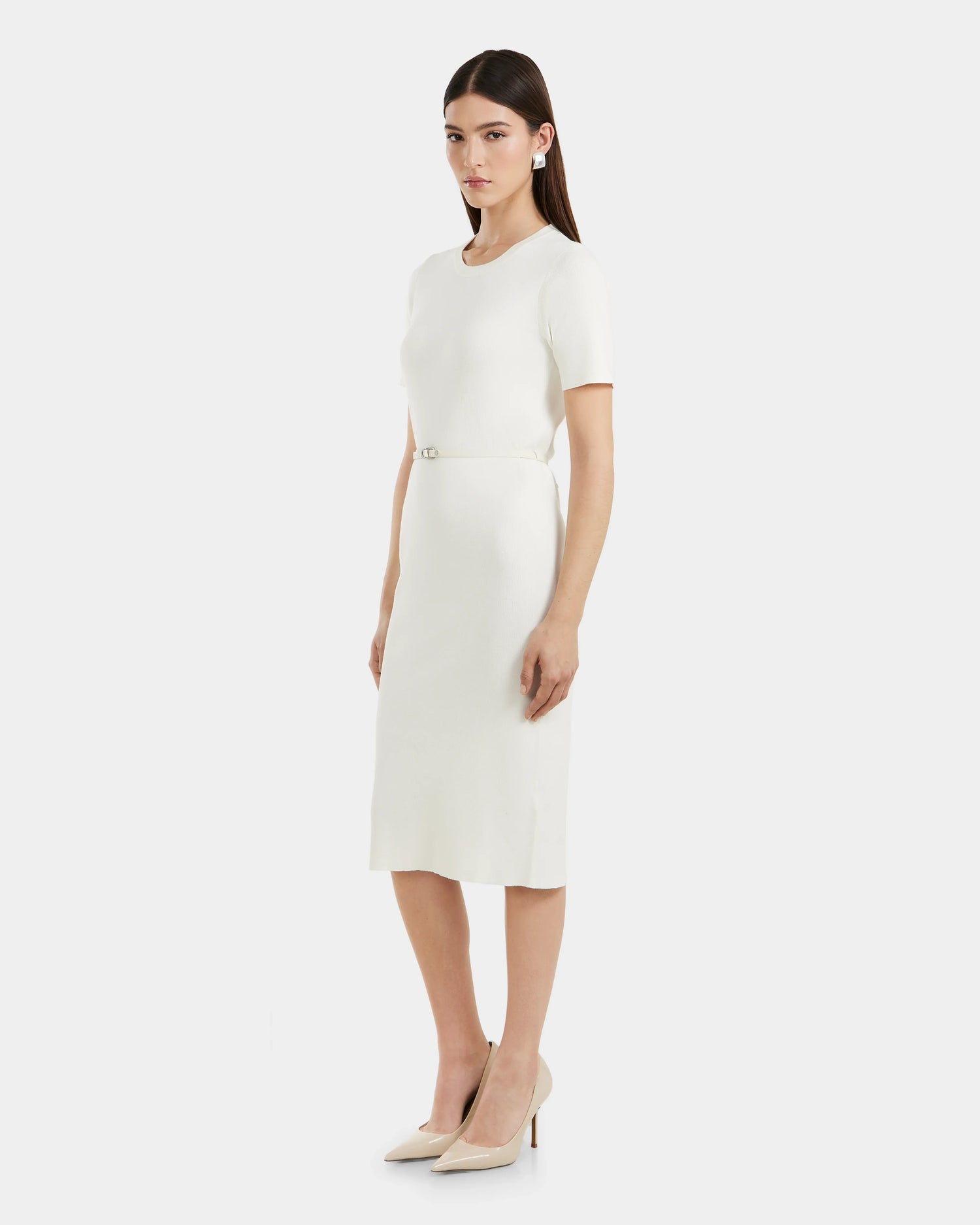 A woman wears the Rudsak PHYLLIS - 8525043 Iceland, a white relaxed-fit dress with a vegan leather waist belt and nude heels, standing against a plain light background and facing slightly to the side with a neutral expression.
