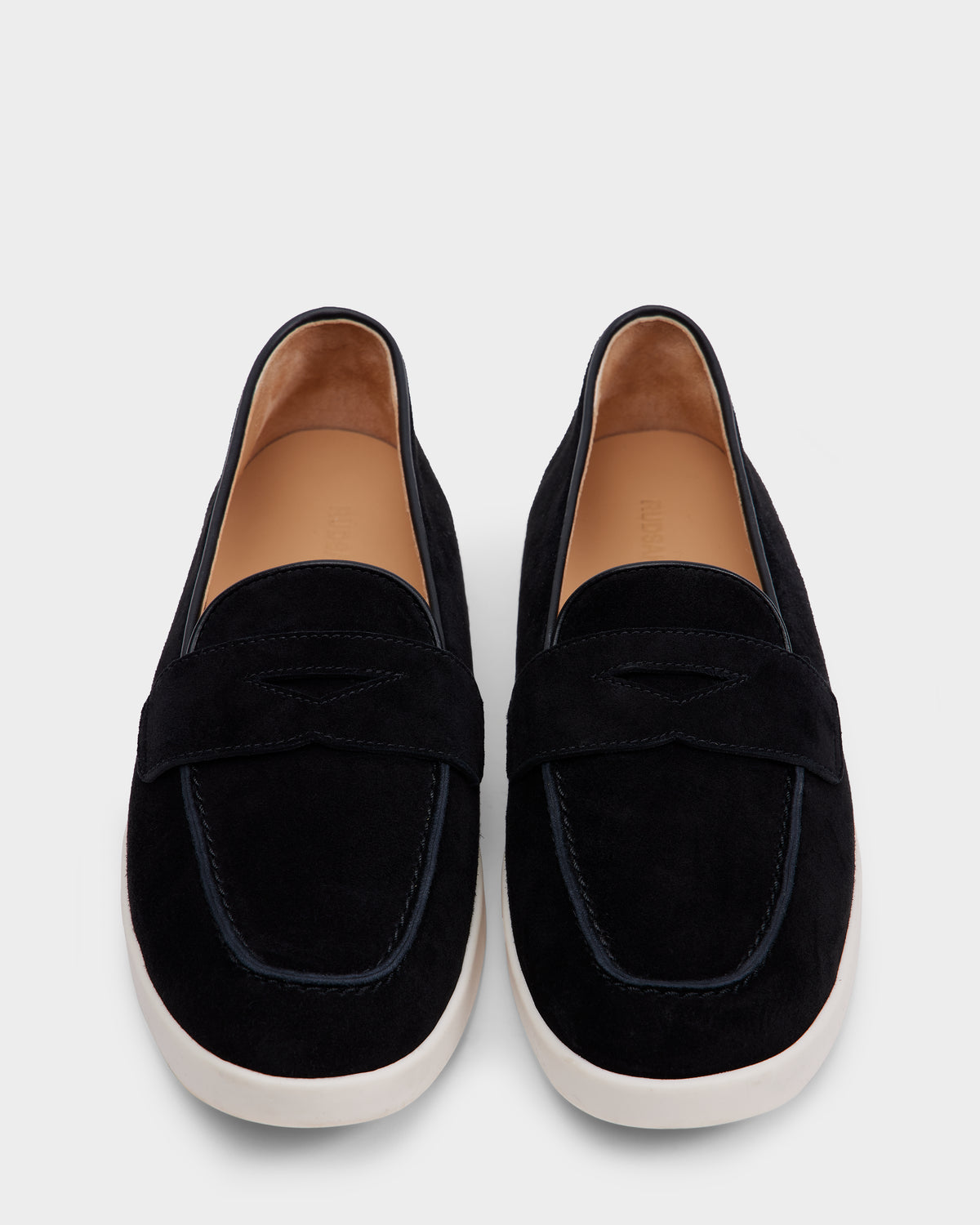 The RABECCA - 8225006 Black loafers by Rudsak feature black suede, white rubber soles, tan insoles, and a decorative strap. These slip-ons blend modern comfort and style, showcased elegantly against a light gray background.
