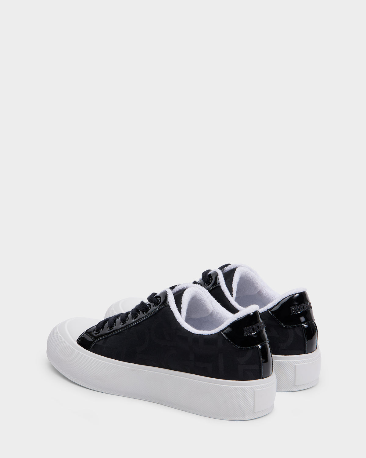 A pair of Rudsak RIMA - 8225001 Black Pattern vegan leather sneakers with glossy black finish, white soles, and white lining is displayed on a light gray background, featuring distinctive branding on the back heel.