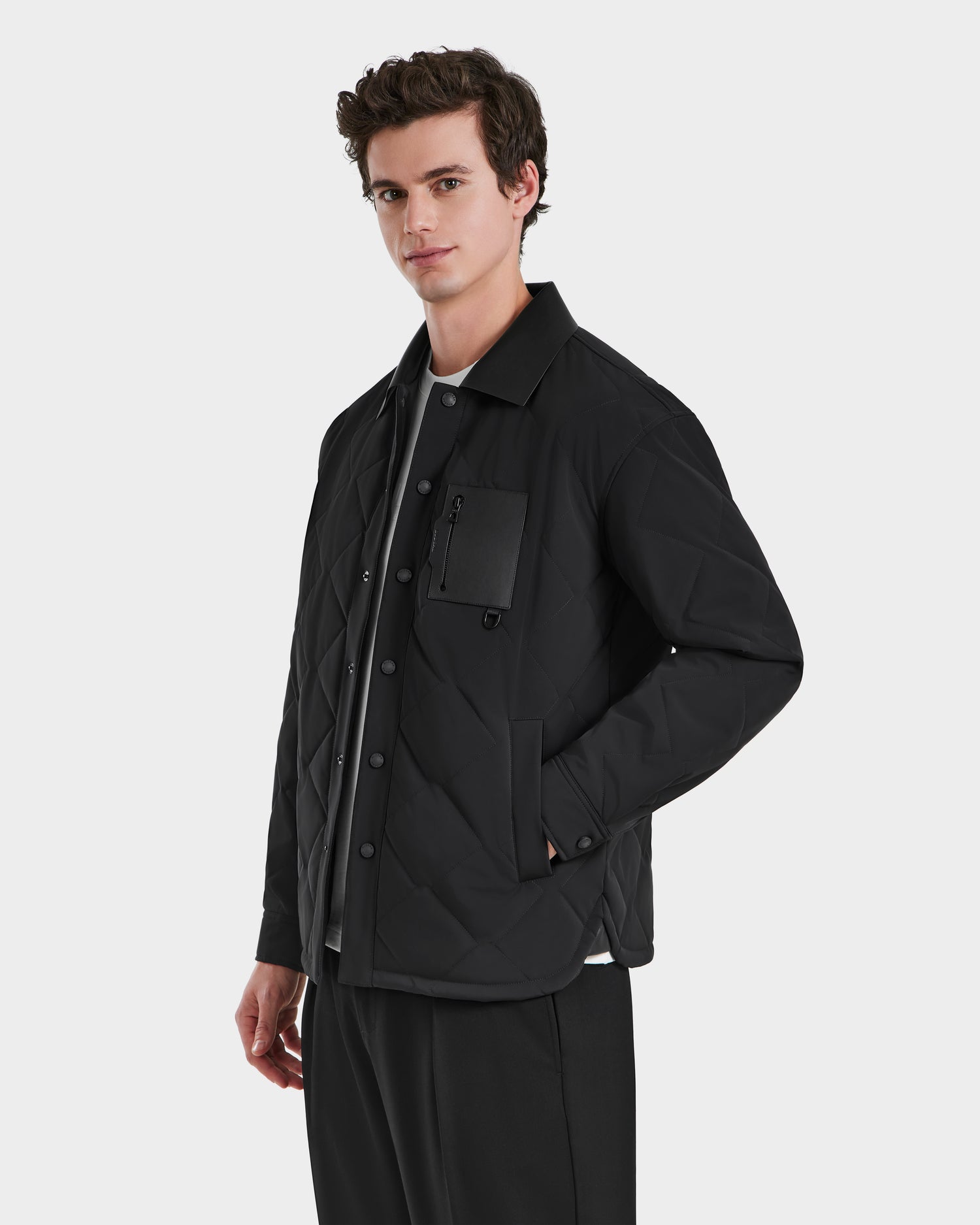 A man models the Rudsak RYAN - 6125023 Black jacket, featuring eco-friendly insulation and a zippered chest pocket, standing against a white background with one hand in his pocket and looking slightly to the side.