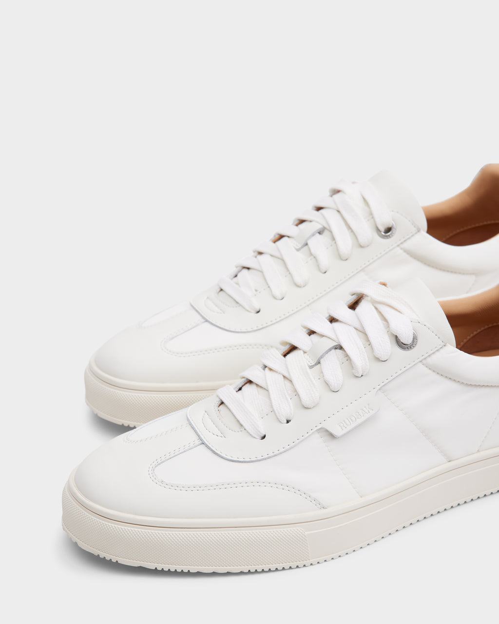 The Rudsak SKYLER - 6225003 Iceland sneakers are white minimalist shoes with white laces, textured rubber soles, and light tan inner linings, displayed on a white background—perfect for clean, comfortable everyday wear.