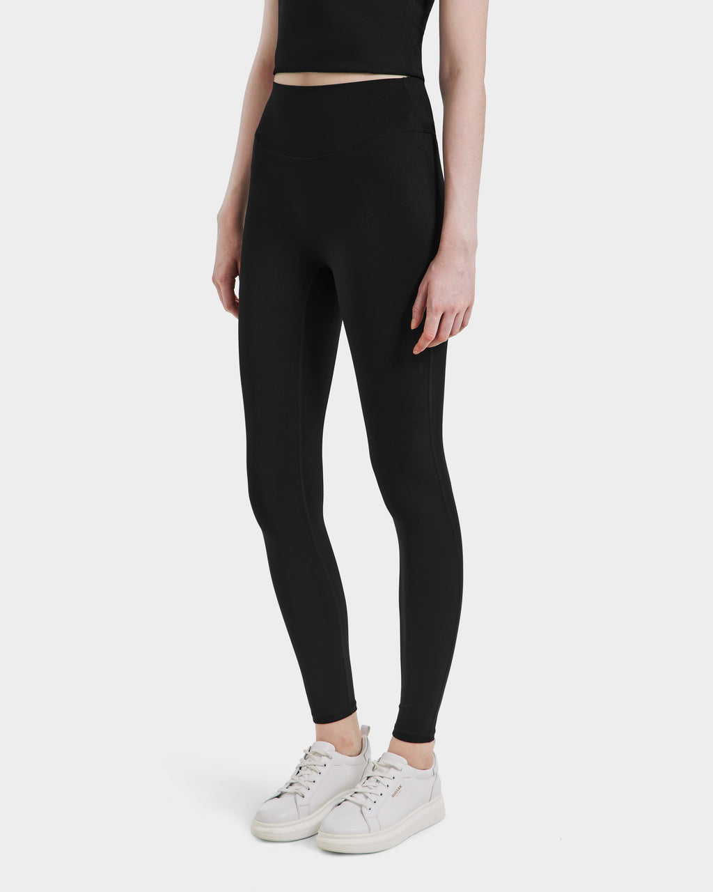 A person wears black high-waisted Rudsak SONOMA - 8525071 leggings, a black crop top, and white sneakers while standing against a plain white background, highlighting the activewear’s versatility from shoulders to feet.