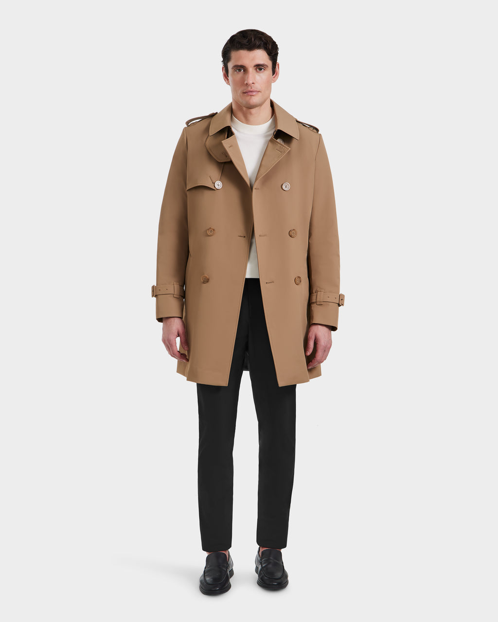 A man faces forward against a plain white background, wearing the Rudsak TIM - 6124025 Camel trench coat over a white shirt, black pants, and black shoes.