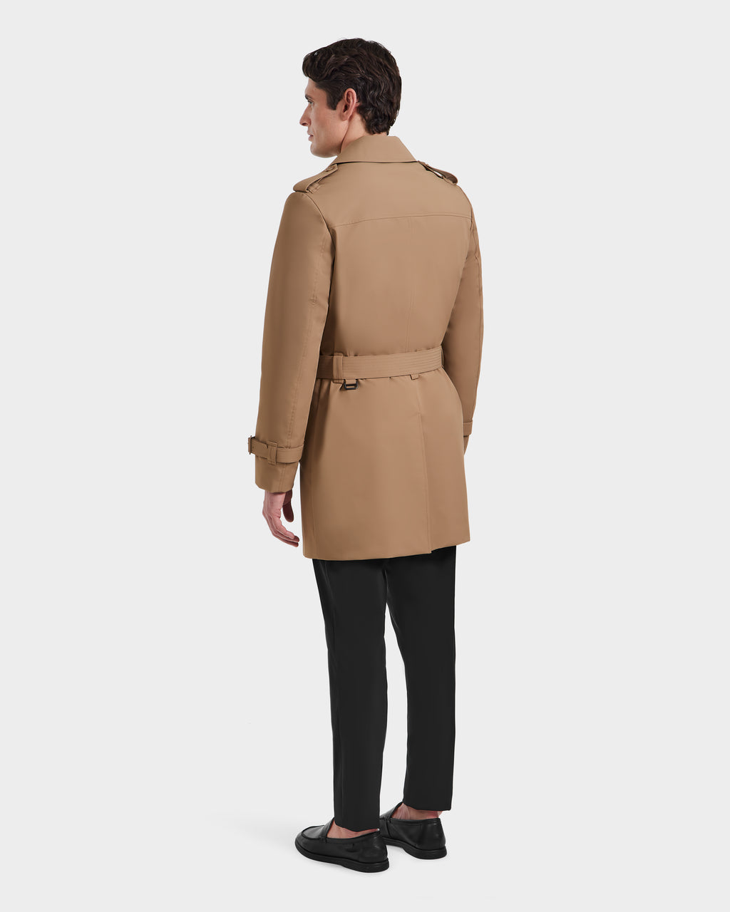 A man, facing away, wears the Rudsak TIM - 6124025 Camel trench coat with a belt, styled with black pants and shoes against a plain white background.