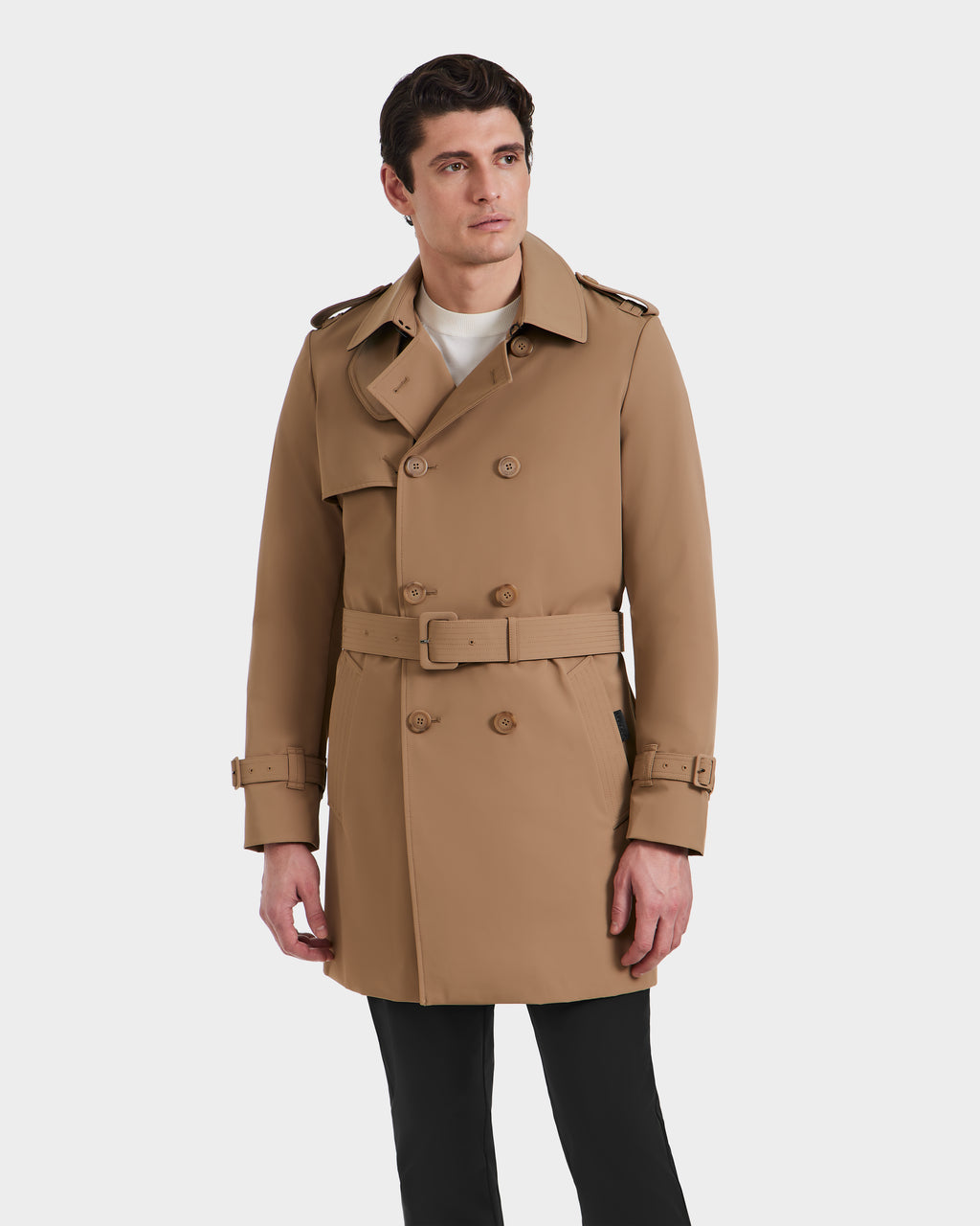 A man wearing the Rudsak TIM - 6124025 Camel trench coat with a belt and epaulets, paired with black pants, stands against a plain white background.