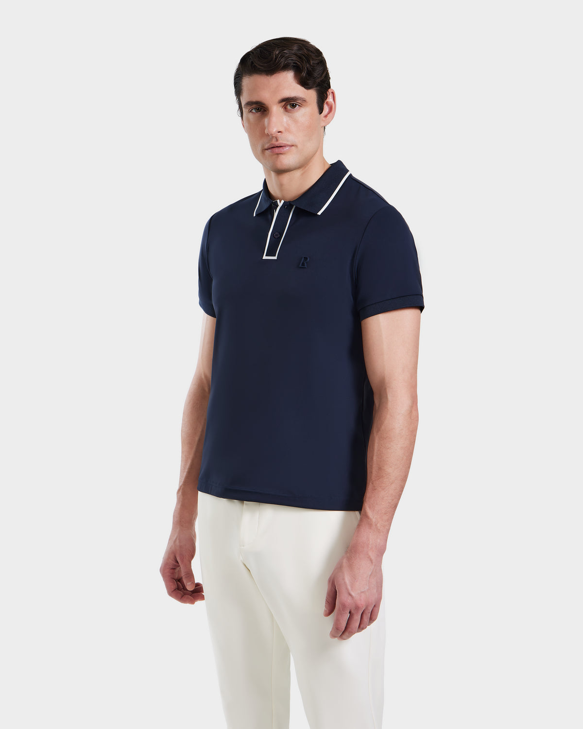 A man wears the XAVIER - 6524027 Navy polo by Rudsak, featuring white trim on the collar and sleeves, paired with white pants against a plain white background.