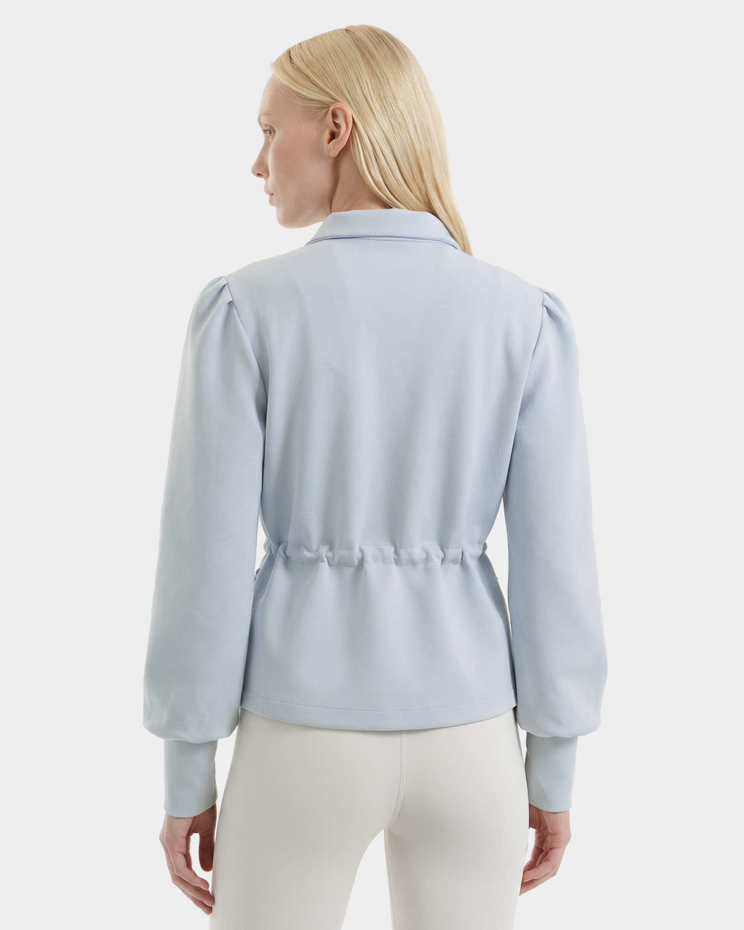 A woman with straight blonde hair is shown from the back, wearing the Rudsak ELODIE - 8526039 Powder Blue lightweight blouse and white pants, standing against a plain white background.