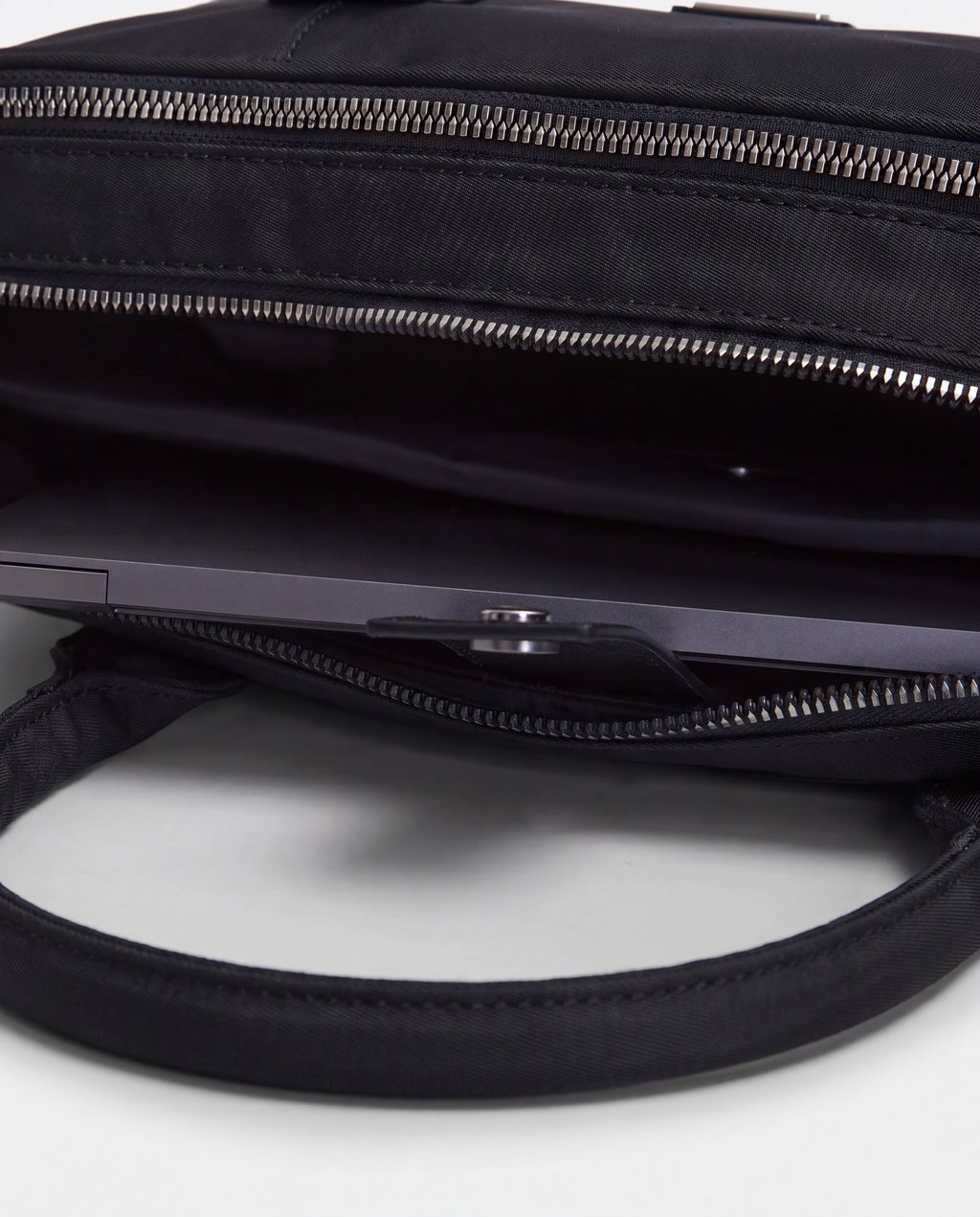 A close-up view of the Rudsak HENRY N - 9326056 Black bag with its open top reveals a laptop partially tucked inside the main compartment, while the bag’s handles are prominently visible in the foreground.