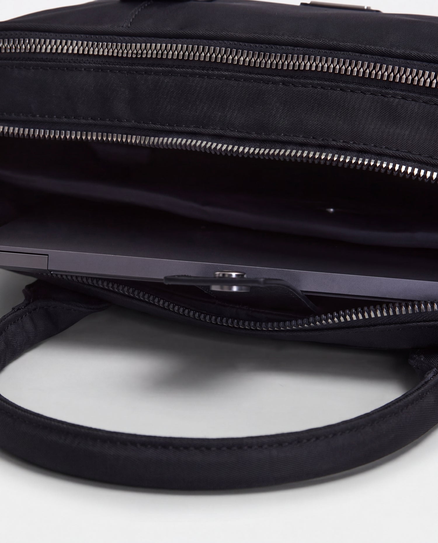 A close-up view of the Rudsak HENRY N - 9326056 Black bag with its open top reveals a laptop partially tucked inside the main compartment, while the bag’s handles are prominently visible in the foreground.