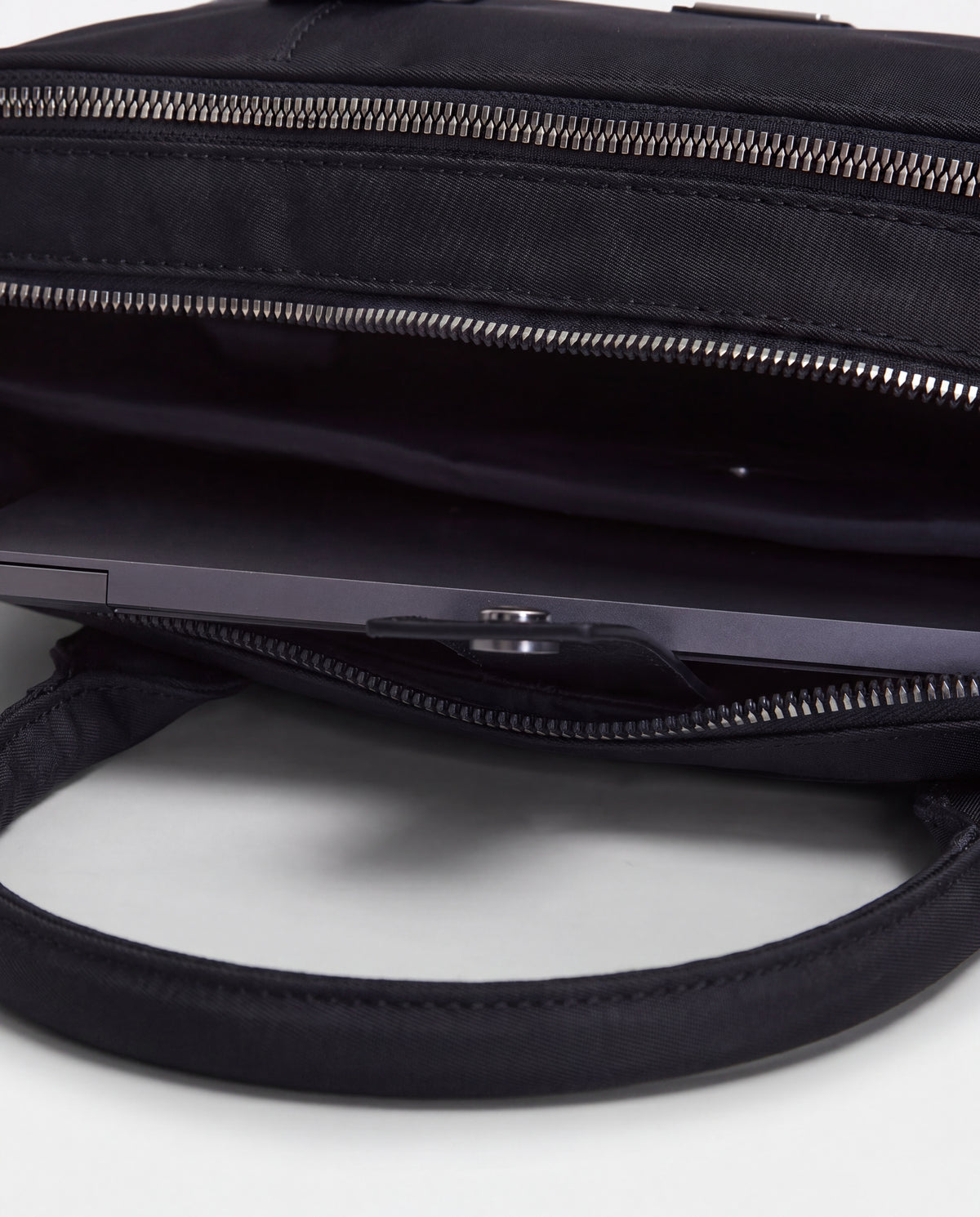 A close-up view of the Rudsak HENRY N - 9326056 Black bag with its open top reveals a laptop partially tucked inside the main compartment, while the bag’s handles are prominently visible in the foreground.