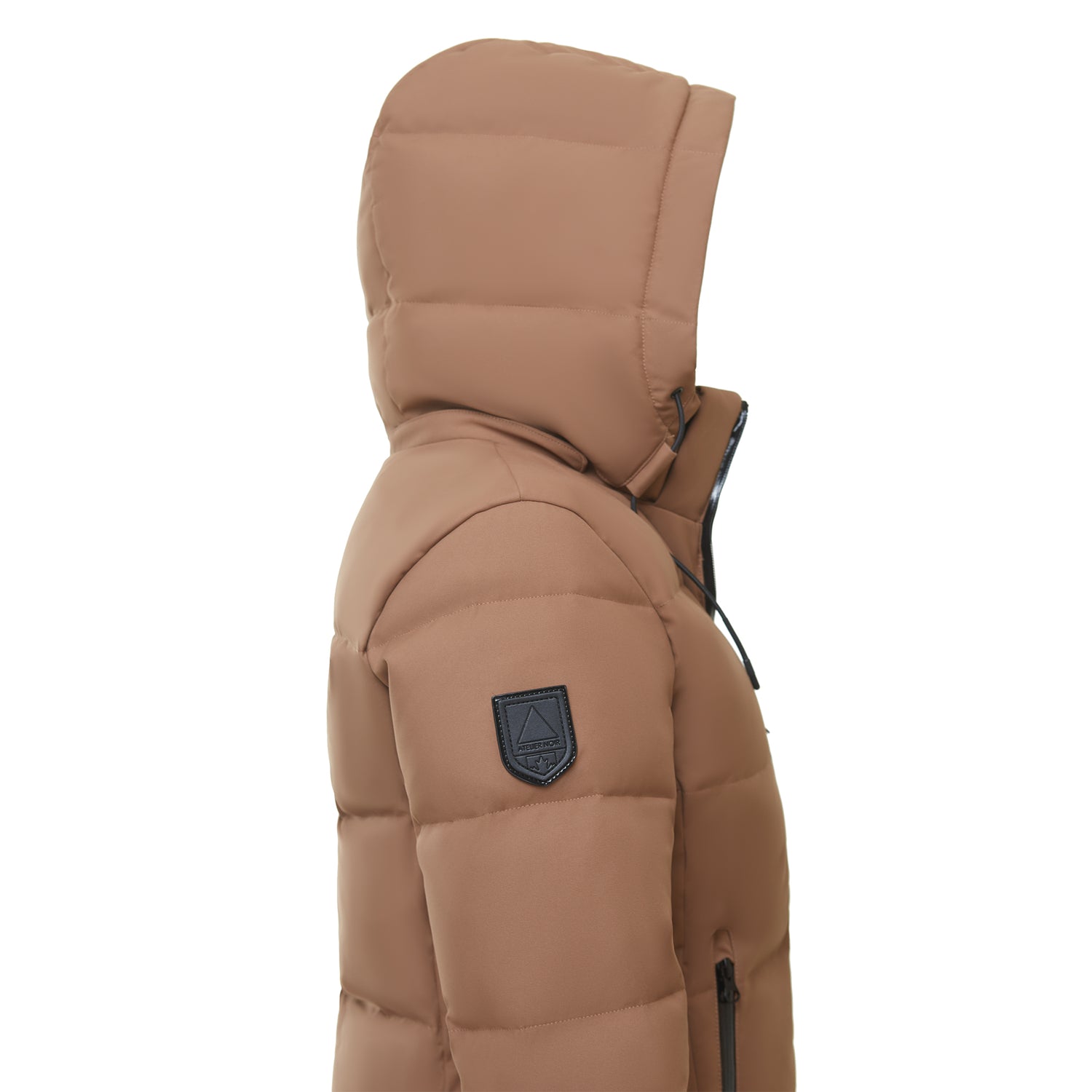 A side view of a person wearing the Rudsak SYDNEY COM - 4123511 Taupe puffer jacket with hood up, black upper sleeve patch, and front zipper. The water-repellent jacket is shown against a plain white background.