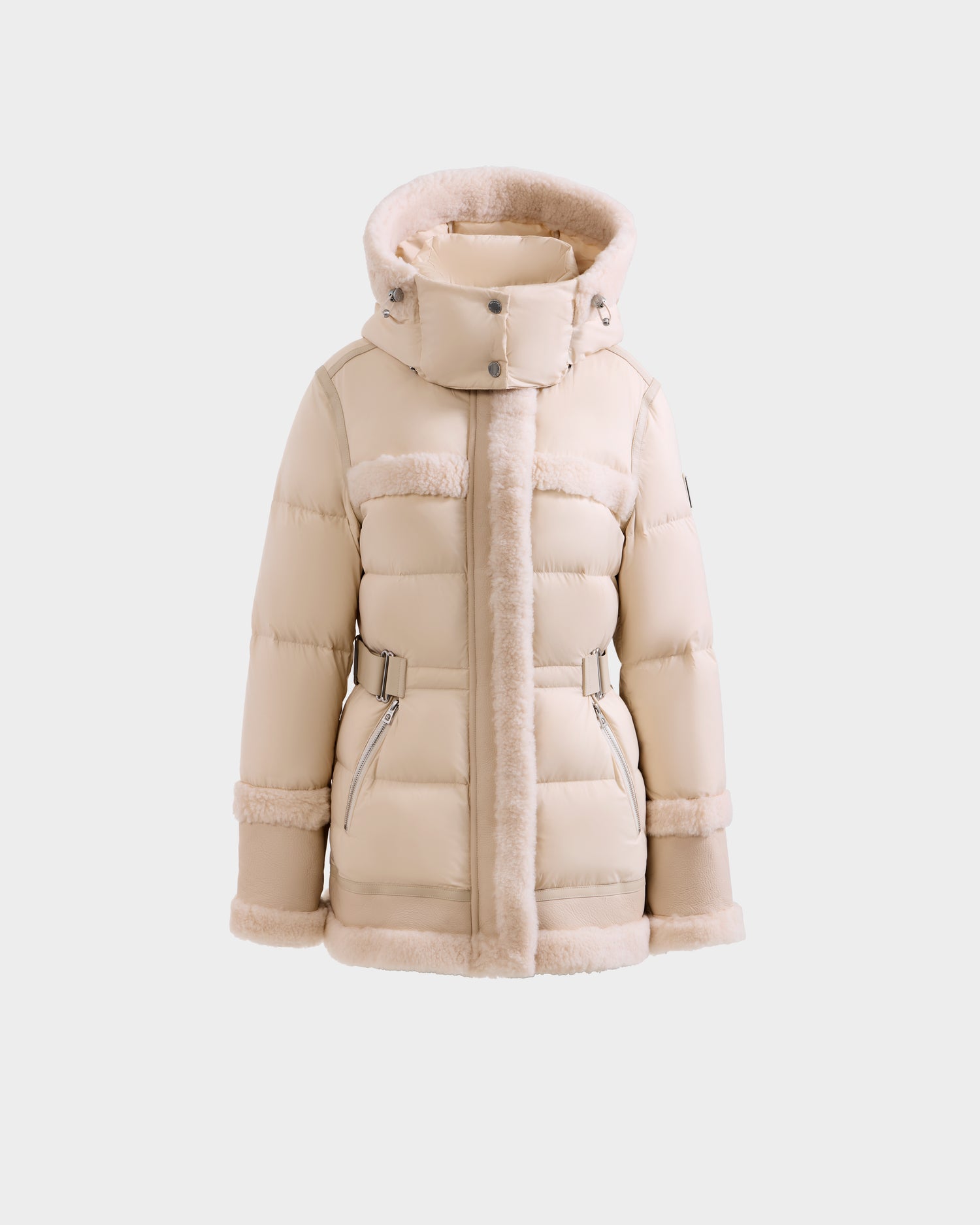 The Rudsak TESSA - 8125615 Vanilla is a beige women’s down puffer jacket with a faux fur hood, front zipper, two zippered pockets, and adjustable waist straps, shown on a plain white background.