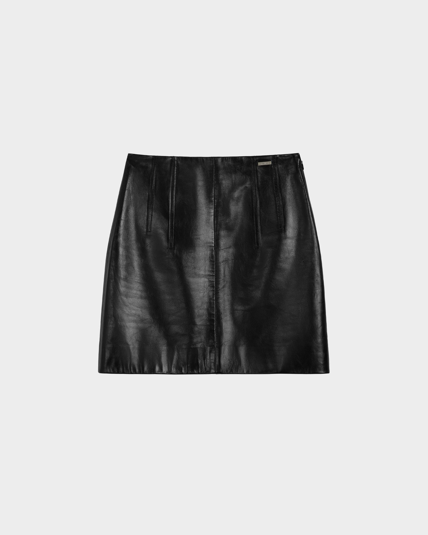 The Rudsak TIA - 8524612 Black women’s leather mini skirt features a shiny black finish, straight cut, and subtle vertical seams, shown on a light gray background. A versatile modern wardrobe piece.
