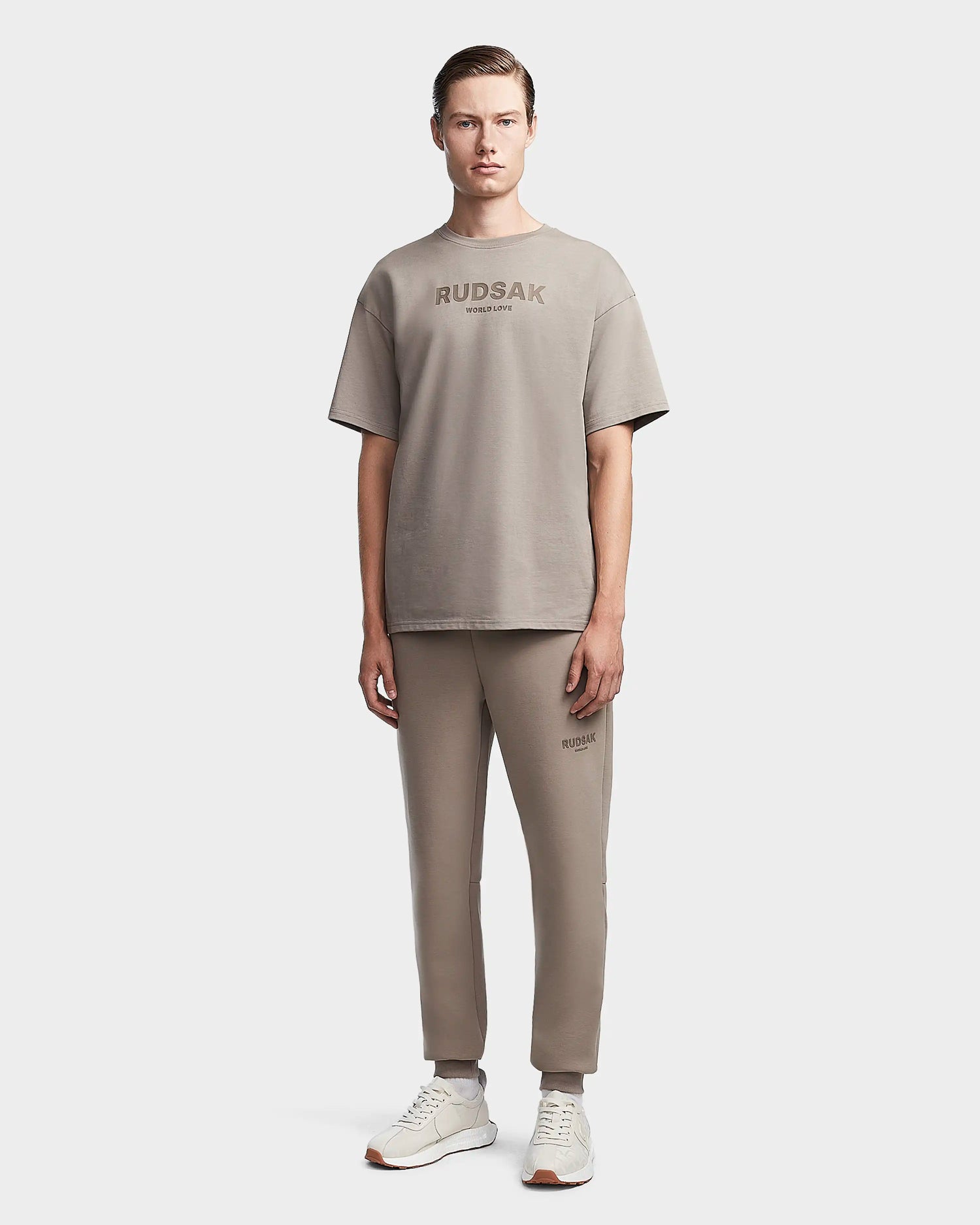 A man faces forward wearing the Rudsak KARTER - 9523520 Cement M premium cotton taupe T-shirt and matching jogger pants with white sneakers, set against a plain white background.
