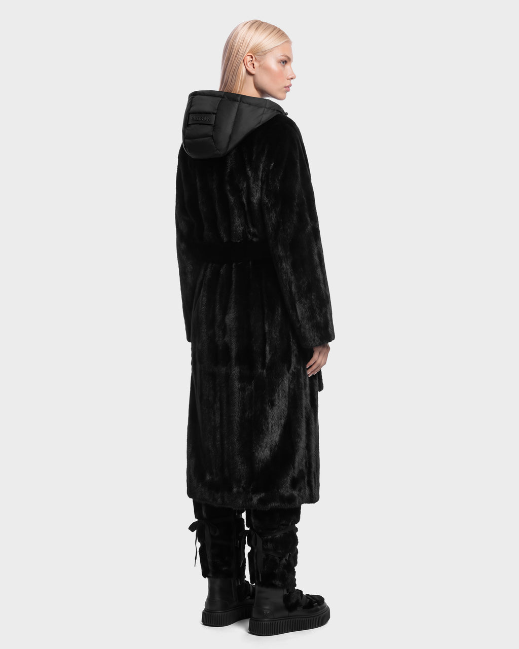 A person seen from behind wears a VIVIENNE - 8126528 Black long faux-fur coat with a hooded puffer collar and black boots for winter city dressing.