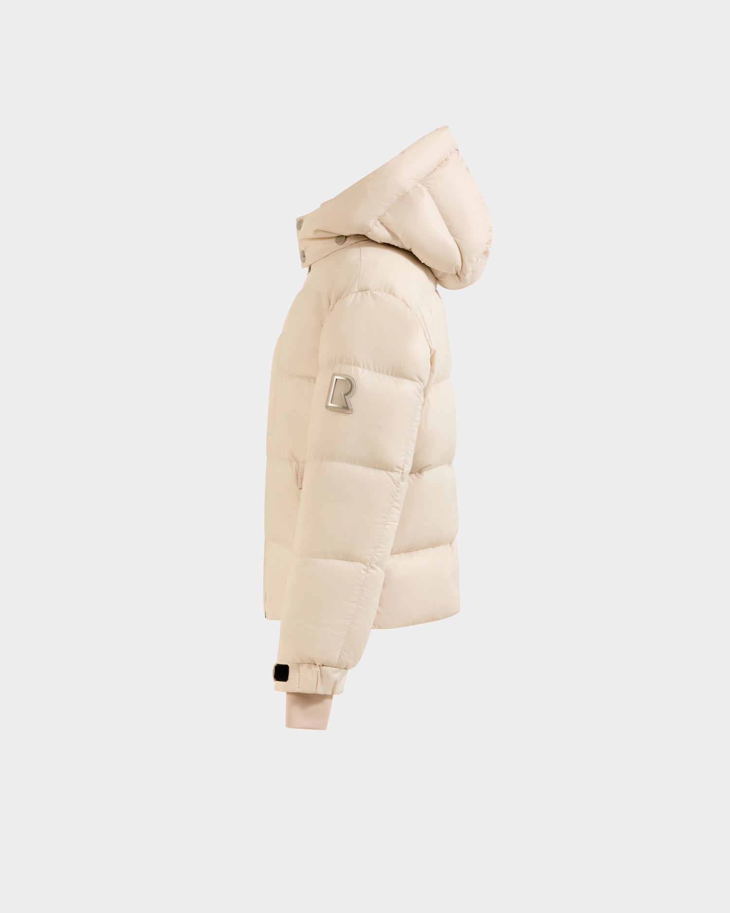 The VINCE KS - 0124502 Vanilla by Rudsak is a beige unisex puffer jacket with a hood, viewed from the side. It features an "R" patch on the upper sleeve, ribbed cuffs, and RDS-certified down filling, set against a light gray background.