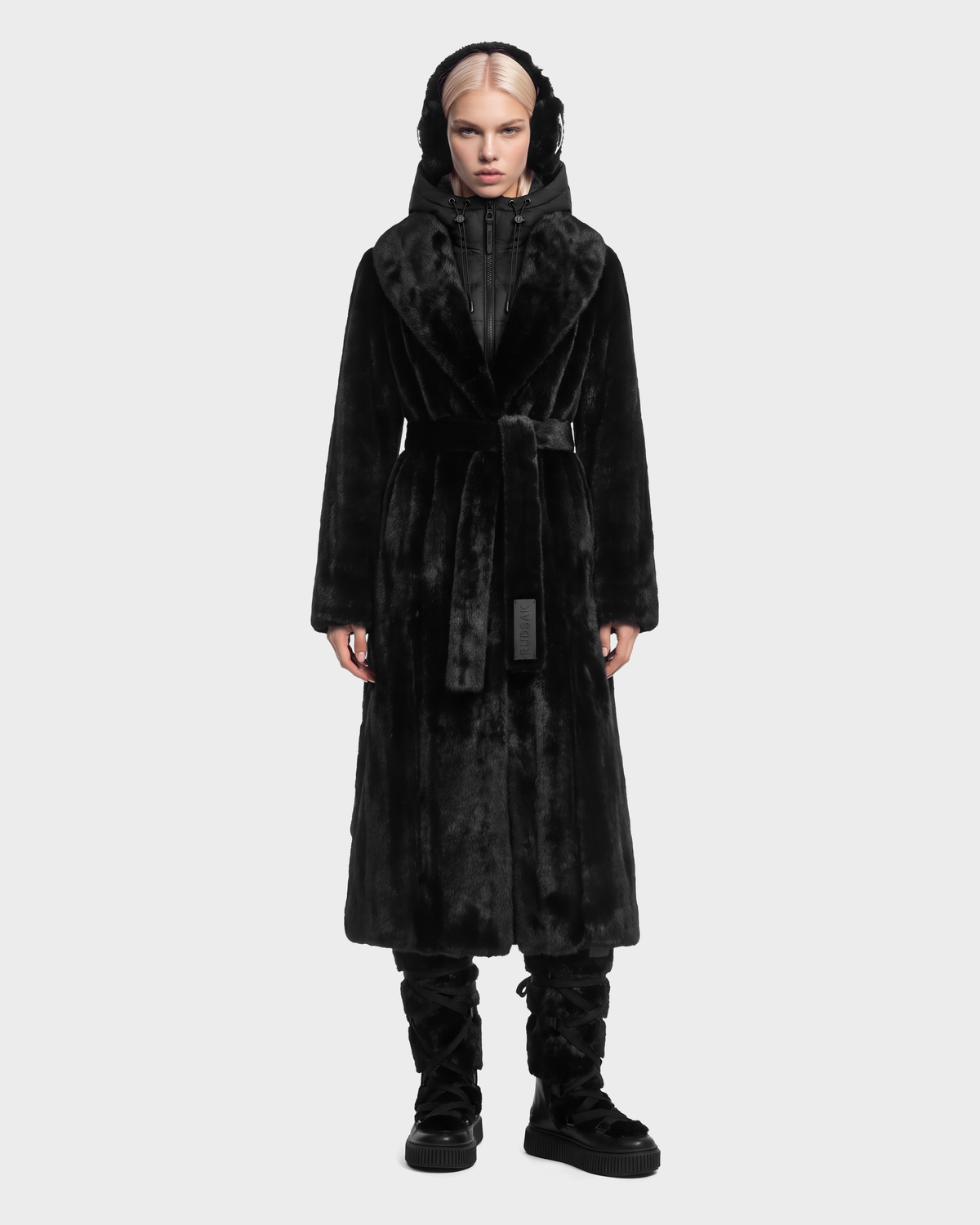 A long black VIVIENNE - 8126528 Black belted faux fur hooded coat layered over a black zip-up jacket and black platform boots.