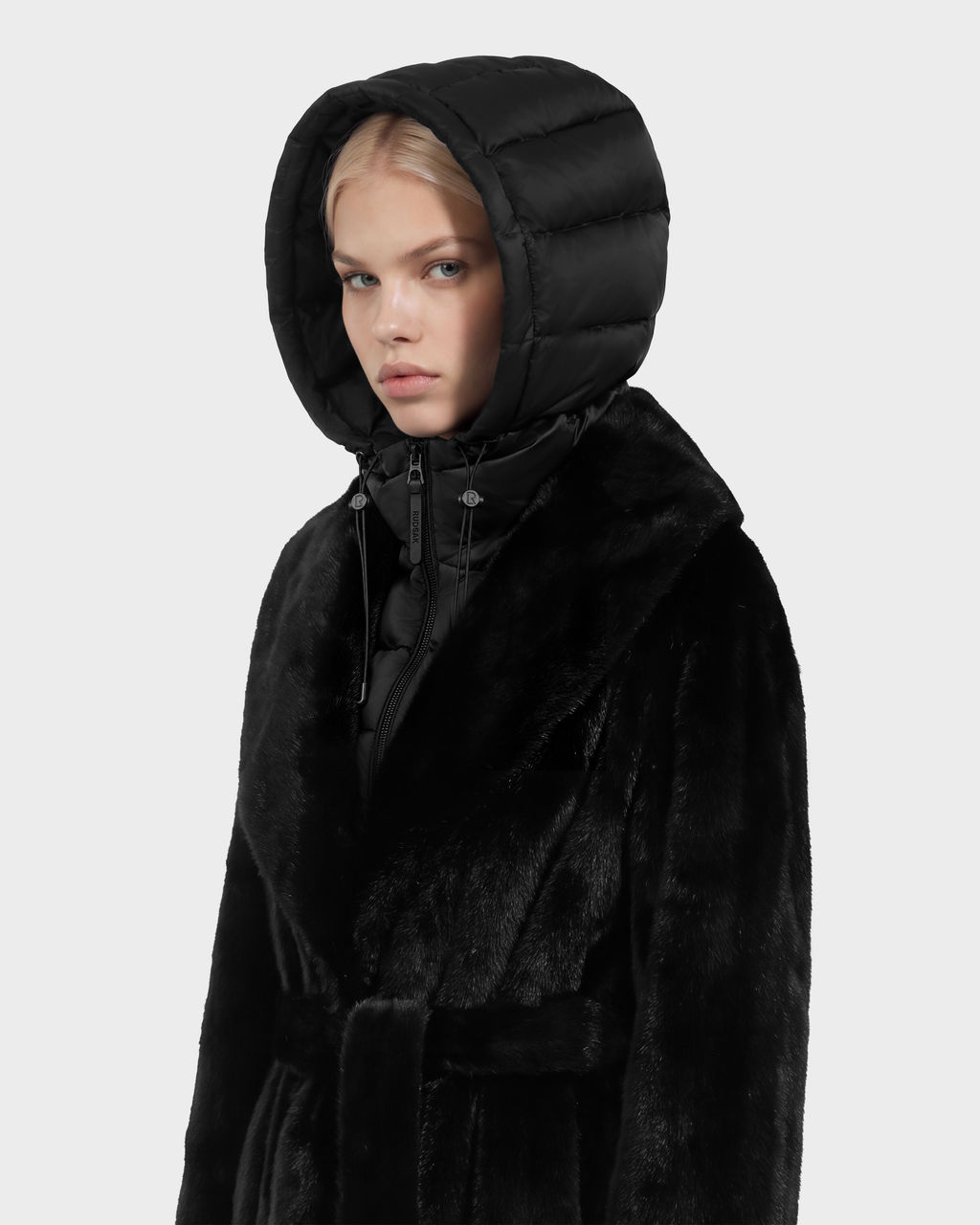 A person wears the VIVIENNE - 8126528 Black faux-fur coat featuring a belted waist and an attached black quilted hood.