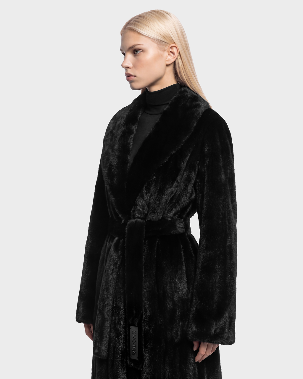 A person wearing a black, belted VIVIENNE - 8126528 Black faux fur coat with a wide collar.