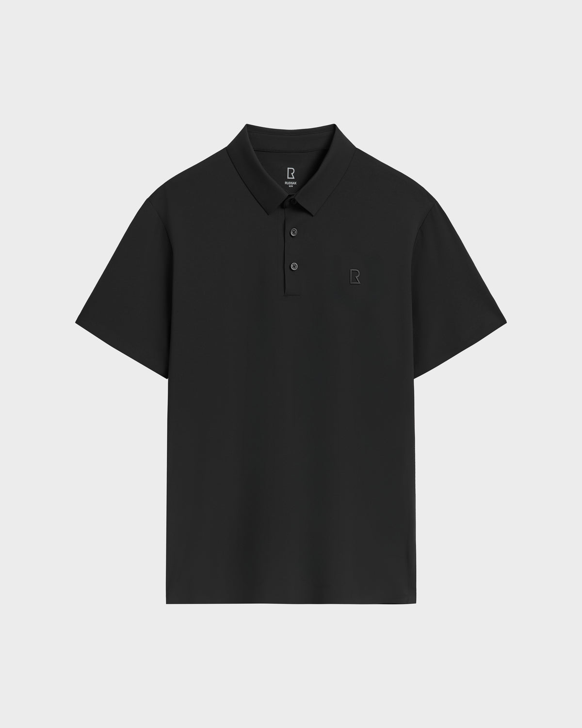 The Rudsak WELLS - 6525017 Black is a mens essential: a tailored-fit, plain black polo with short sleeves, three-button collar, and small square logo on the left chest. Made from lightweight technical fabric. Displayed on a light gray background.