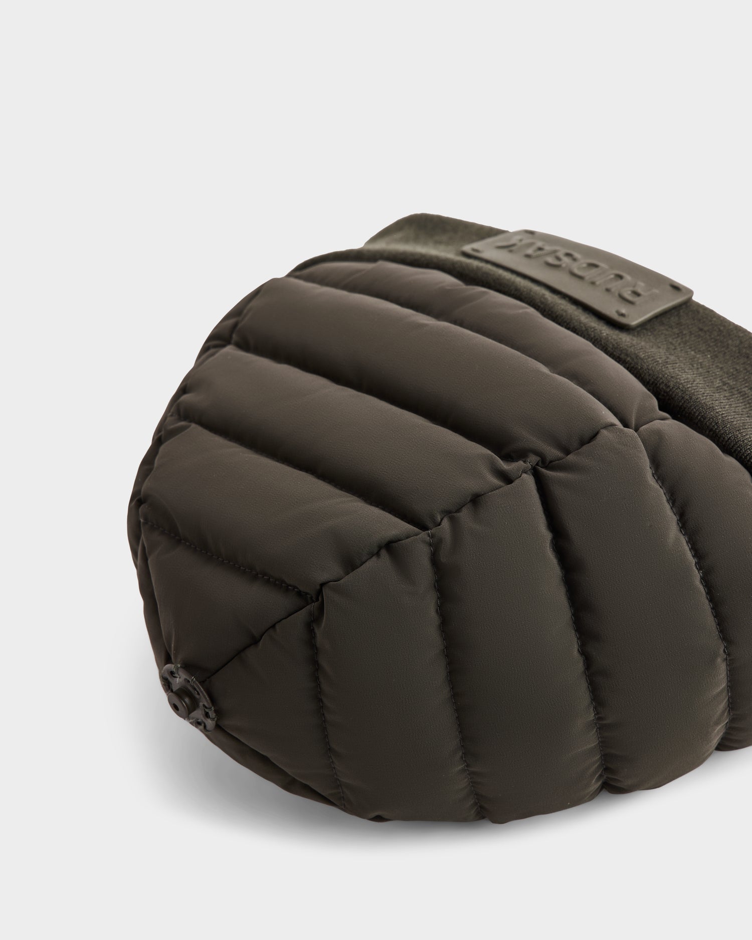 A close-up of the GALA - 8424514 Dark Olive padded, quilted winter ear muff by Rudsak, featuring a soft fabric band and shown with a removable faux fur pom pom on a light background.