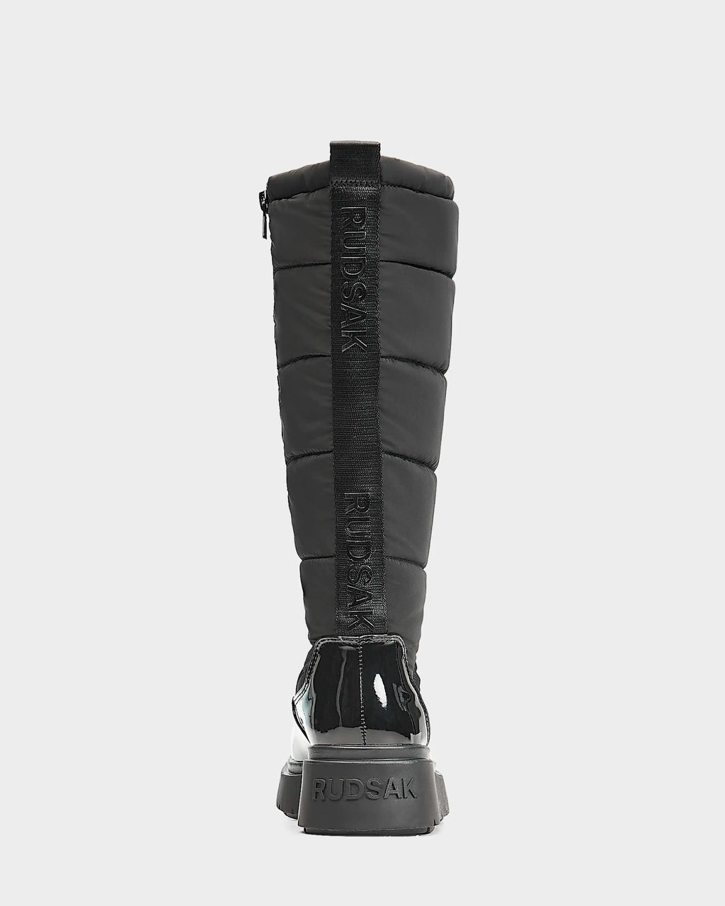 A black, knee-high women's quilted winter boot by Rudsak, CLAUDE - L223506, shown from the back with glossy heel and sole accents, featuring RUDSAK branding vertically on the back strap and heel.