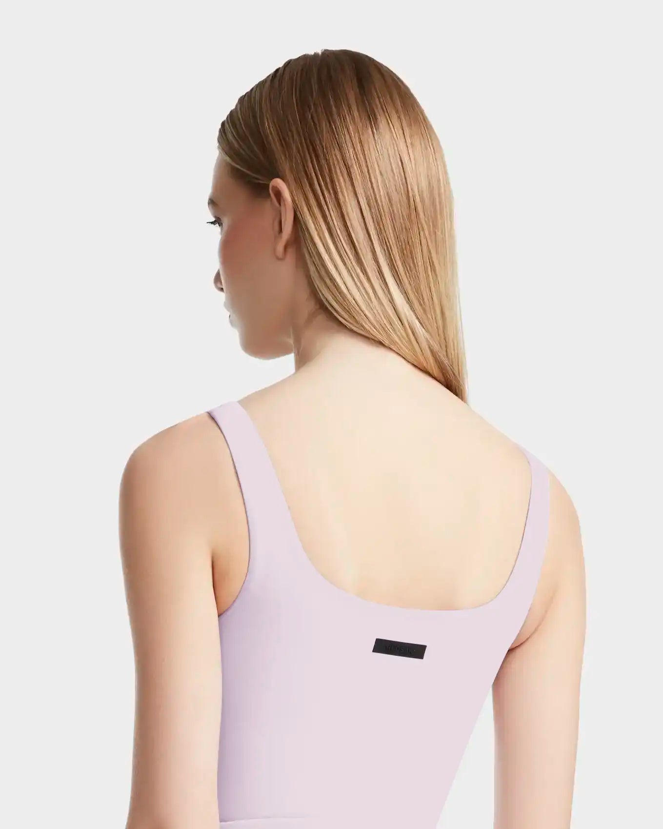 A woman with straight, light brown hair models the Rudsak BRIDGET - 8524033 Lilac Foam tank-style bodysuit, seen from behind against a plain light gray background.
