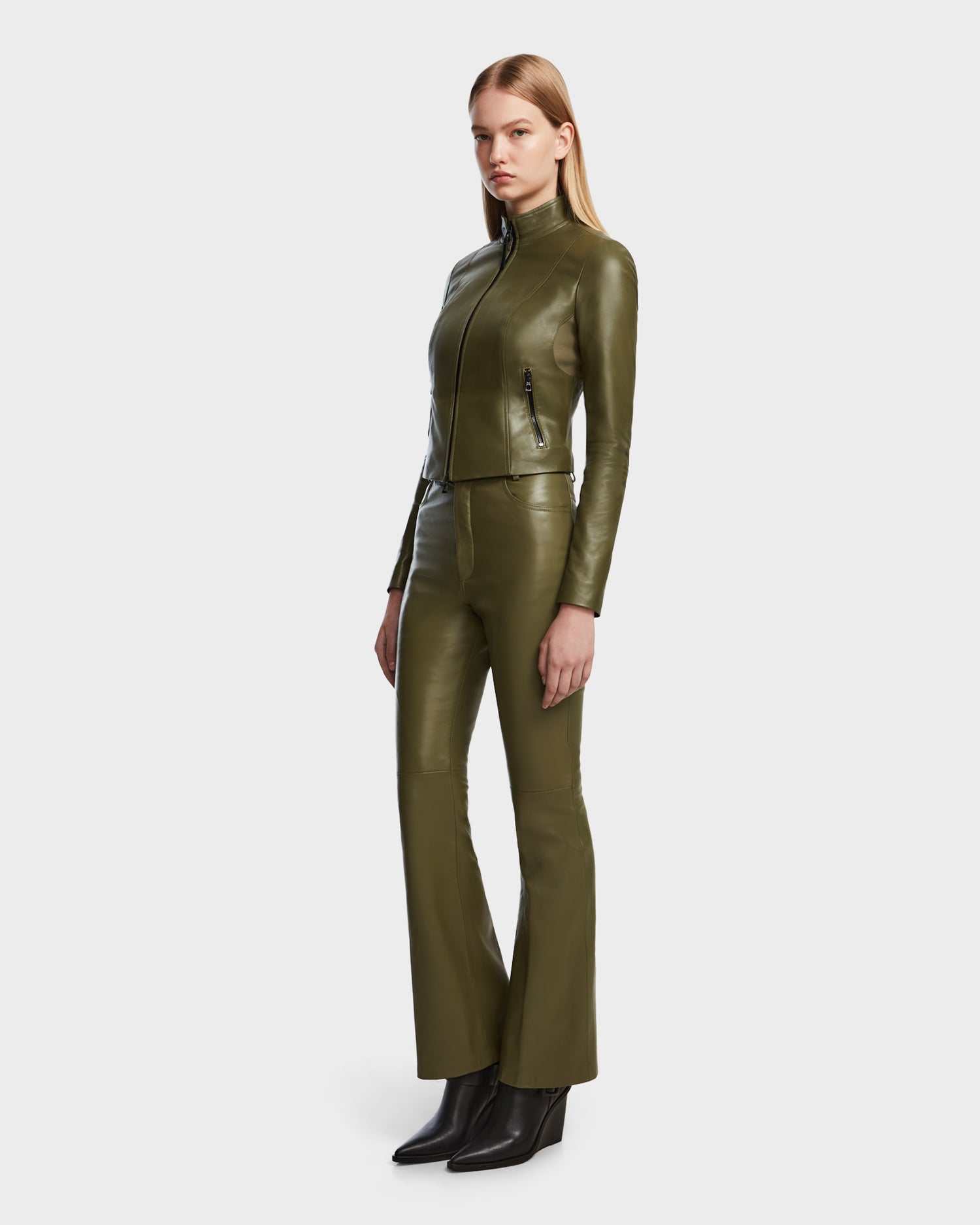 A woman faces slightly sideways in the Rudsak ABIGAIL - 8124560 Loden Green fitted leather jacket and matching olive green pants with black ankle boots, set against a plain light background.
