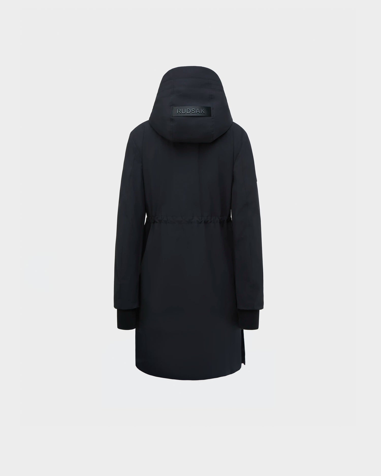 The Rudsak NICOLE - L123002 Black women's rain jacket is displayed from the back, showcasing a hood with a visible RUDSAK logo patch, waist drawstring, long sleeves with ribbed cuffs, and knee-length design against a light background.
