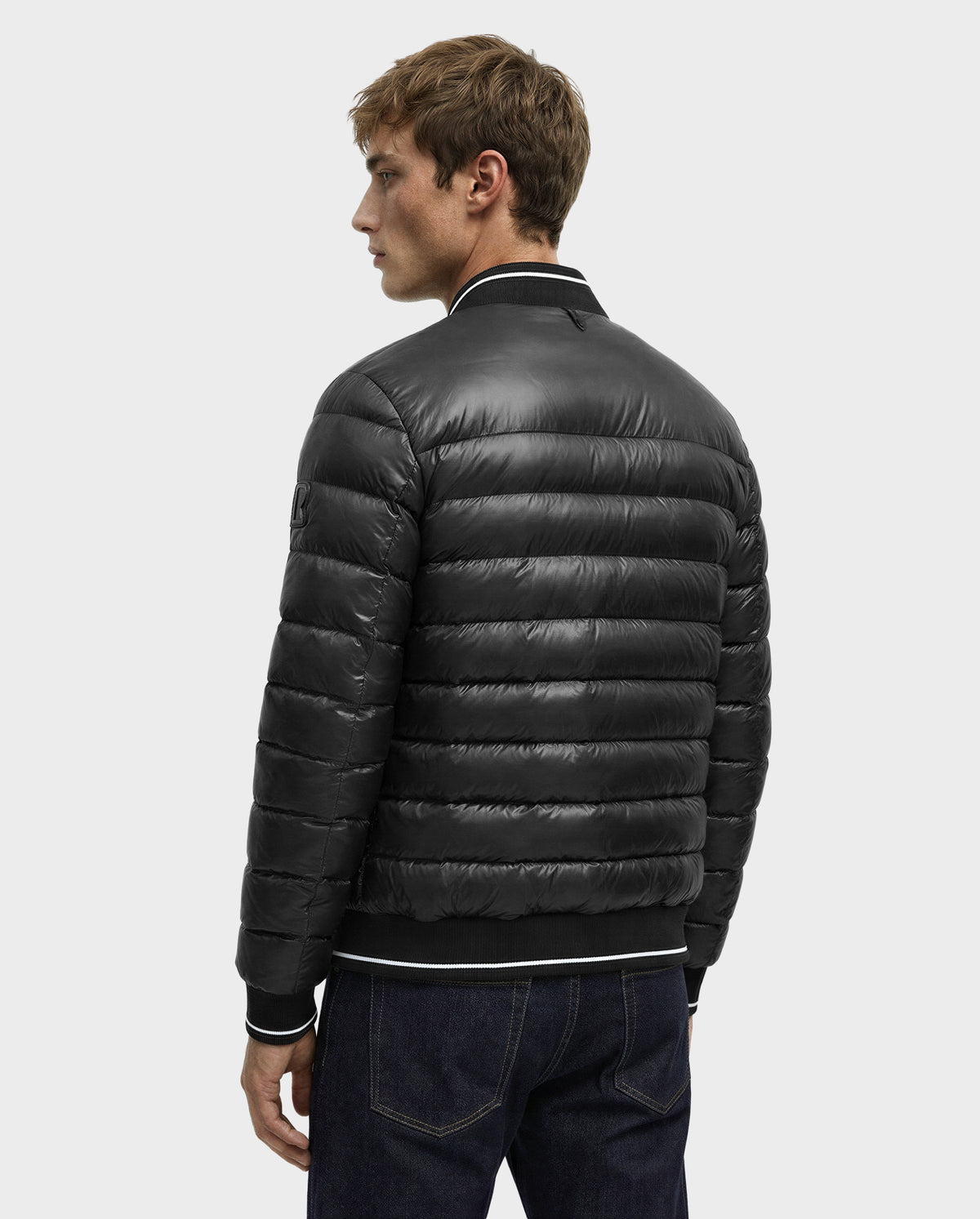 A person wearing the Rudsak JEREMY - 6125025 Black men’s down bomber jacket with premium down insulation and ribbed cuffs and collar is shown from the back, standing against a plain light gray background.
