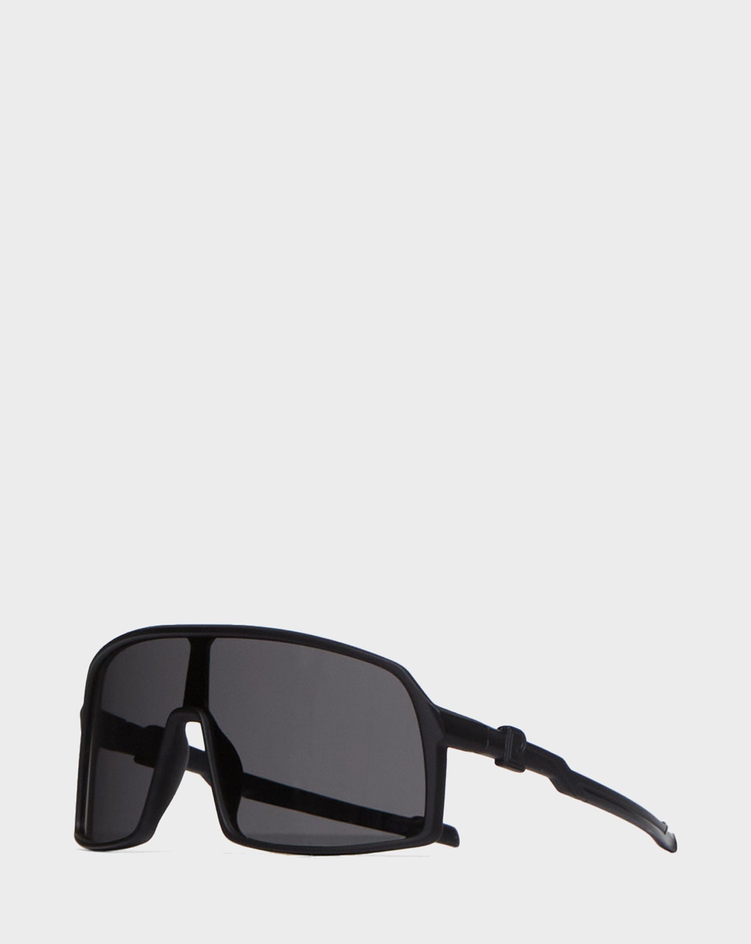 The AKSEL - 9422031 BLACK sunglasses by Rudsak have a black, rectangular shape, UV block lenses, and a thick frame. With dark lenses and flexible curved arms, they combine style and comfort. Shown on a plain light gray background.