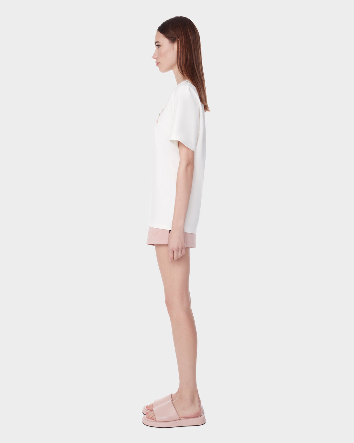 A woman stands in profile against a plain background, wearing the DIAR - 9523003 W OPTIC WHITE top by Rudsak, paired with pink shorts and pink slide sandals.