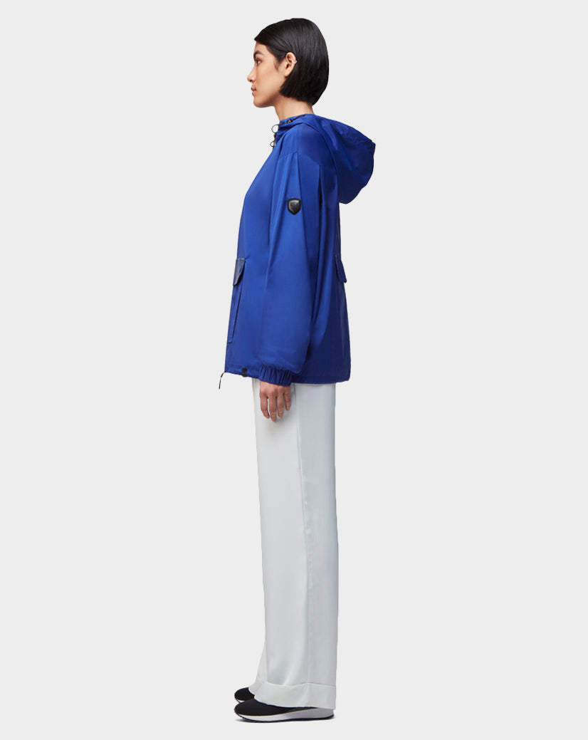 A woman in profile models the Rudsak STALENS - CA EN 9520000 ROYAL BLUE hoodie windbreaker with white wide-leg pants and black shoes against a plain light background, capturing a chic athleisure vibe.