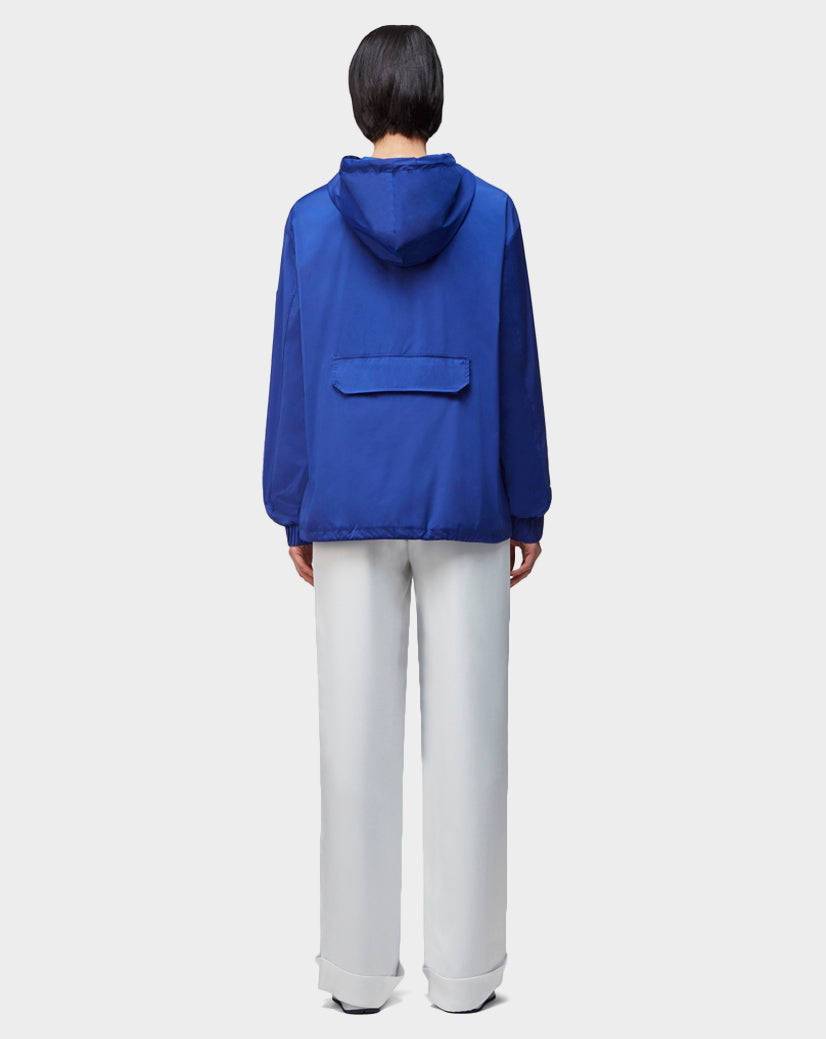 A person is shown from behind wearing the Rudsak STALENS - CA EN 9520000 ROYAL BLUE unisex hoodie windbreaker with a back flap pocket and loose white pants, set against a plain light gray background.