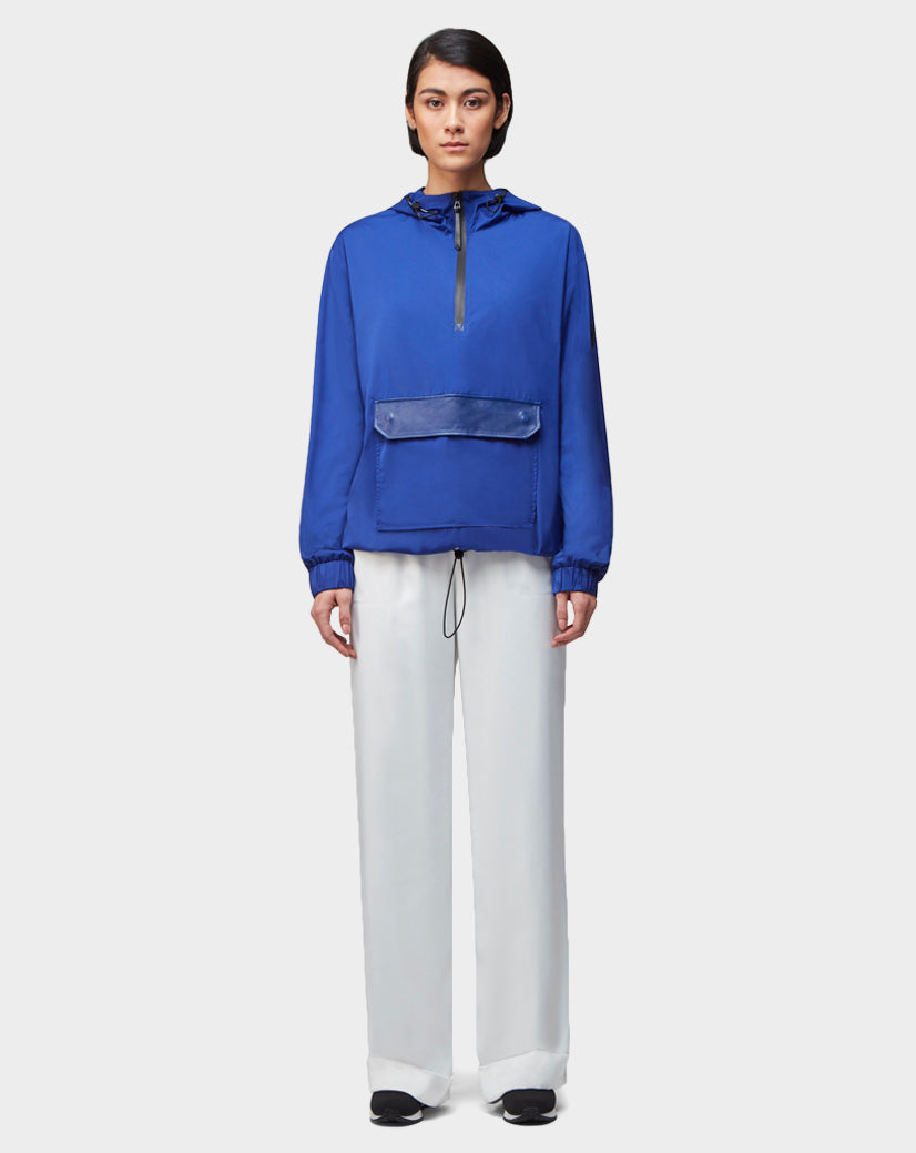 A person faces forward against a light gray background, wearing the Rudsak STALENS - CA EN 9520000 royal blue unisex pullover hoodie windbreaker, loose white pants, and black shoes.