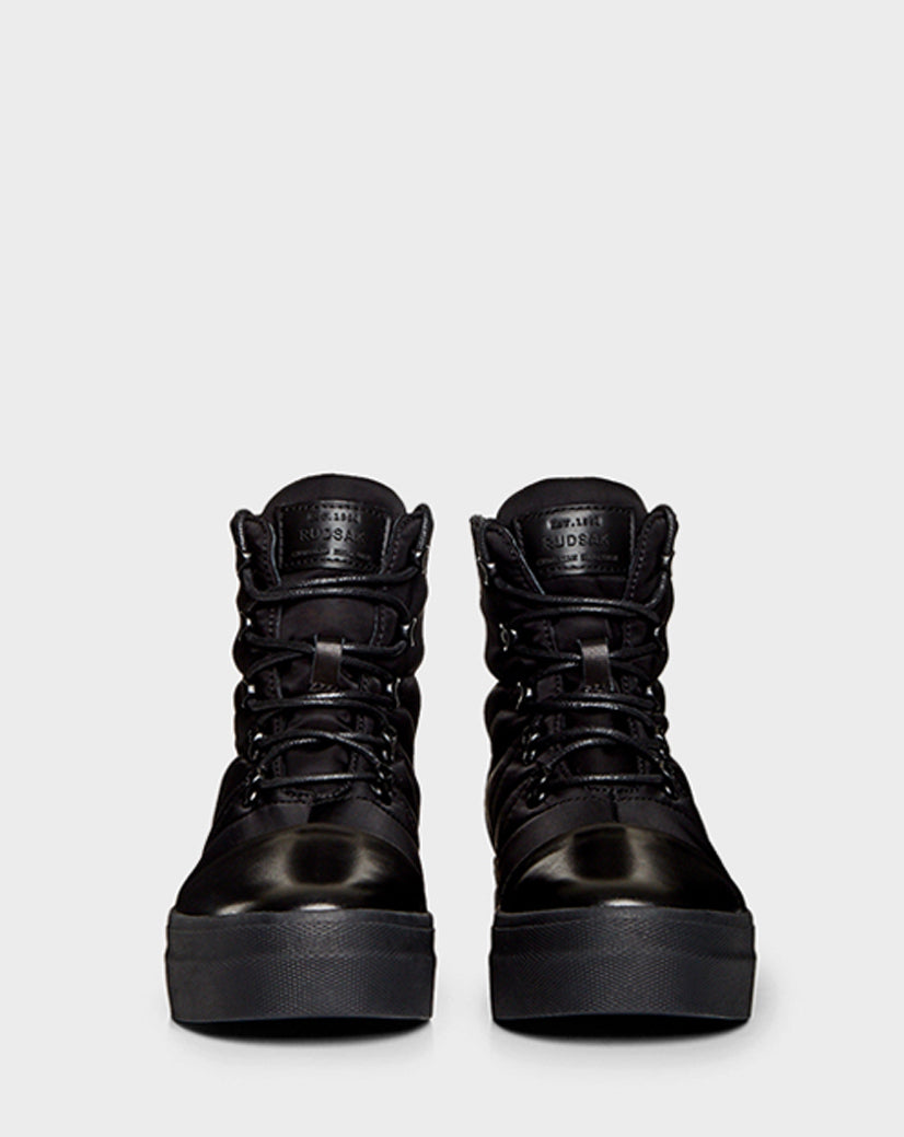 The Rudsak TASSEL - CA EN 8219514 BLACK is a pair of black high-top sneakers with thick soles and laces, resembling winter boots, shown from the front against a plain light gray background.