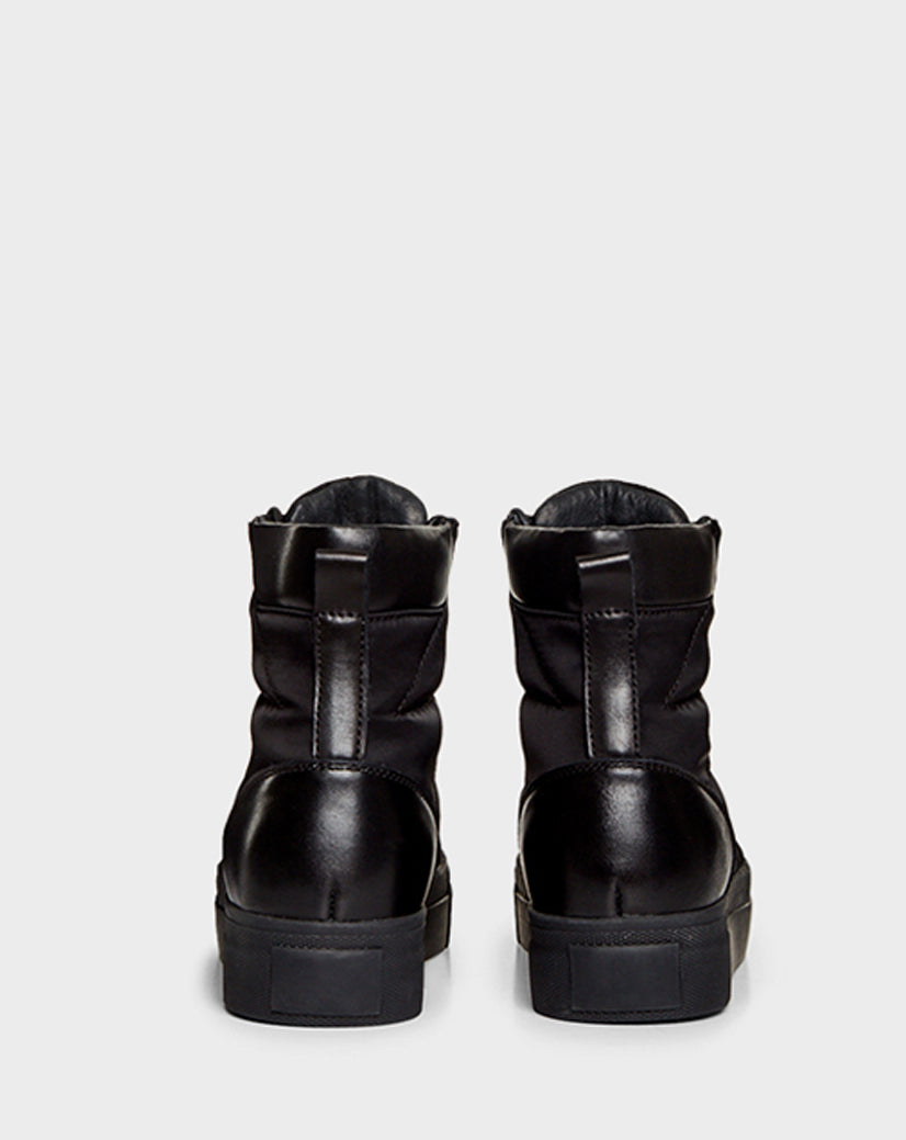 The Rudsak TASSEL - CA EN 8219514 BLACK high-top sneakers feature thick soles and faux shearling, displayed from the back on a plain light gray background.