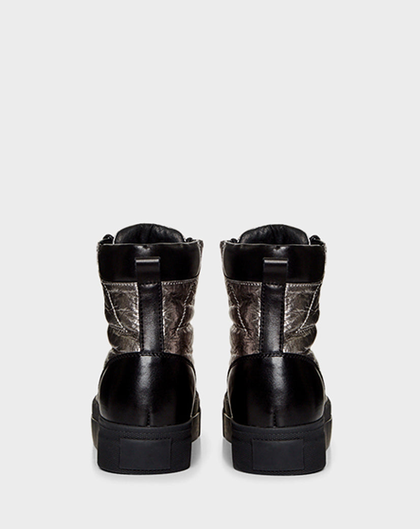 The TASSEL - CA EN 8219514 SILVER sneakers by Rudsak feature a black high-top design with textured, shiny panels and thick soles, reminiscent of winter boots. Shown from the back against a plain light gray background.