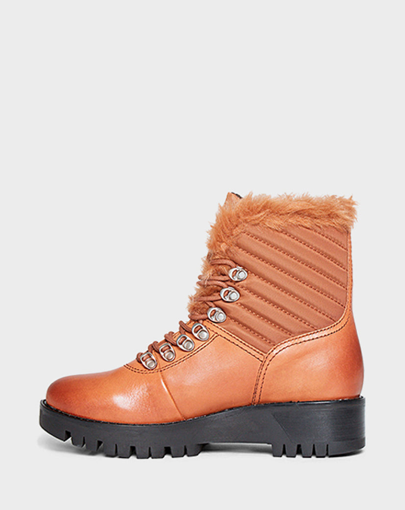 The TSARY - CA EN L219530 TAN by Rudsak is a tan hiking boot with a black chunky sole, metal eyelets, quilted side details, and light brown faux-fur lining at the ankle and tongue, shown on a plain white background.