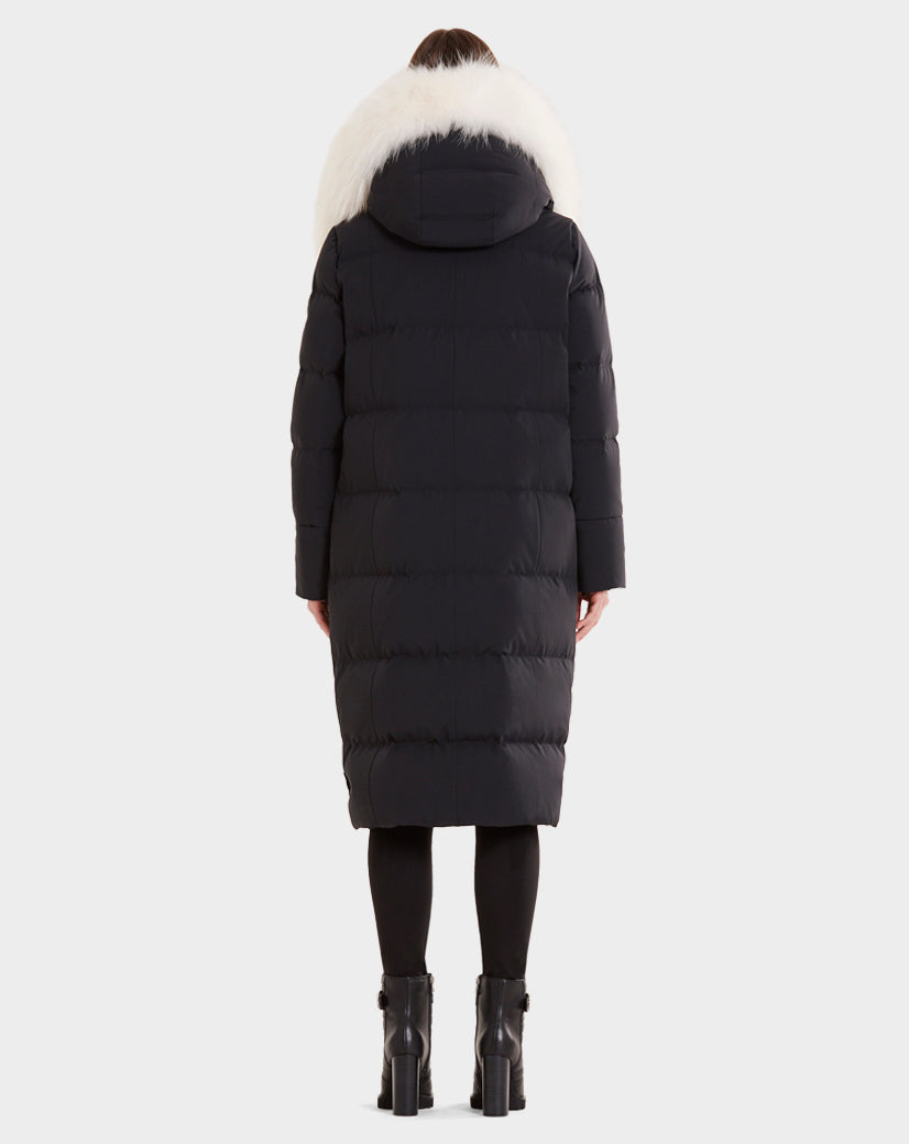 A person models the Rudsak MILANI - CA EN 8119582B BLACK OFF WHITE coat—a long black puffer with an oversized white fur-trimmed hood—seen from the back, paired with black leggings and black heeled boots.