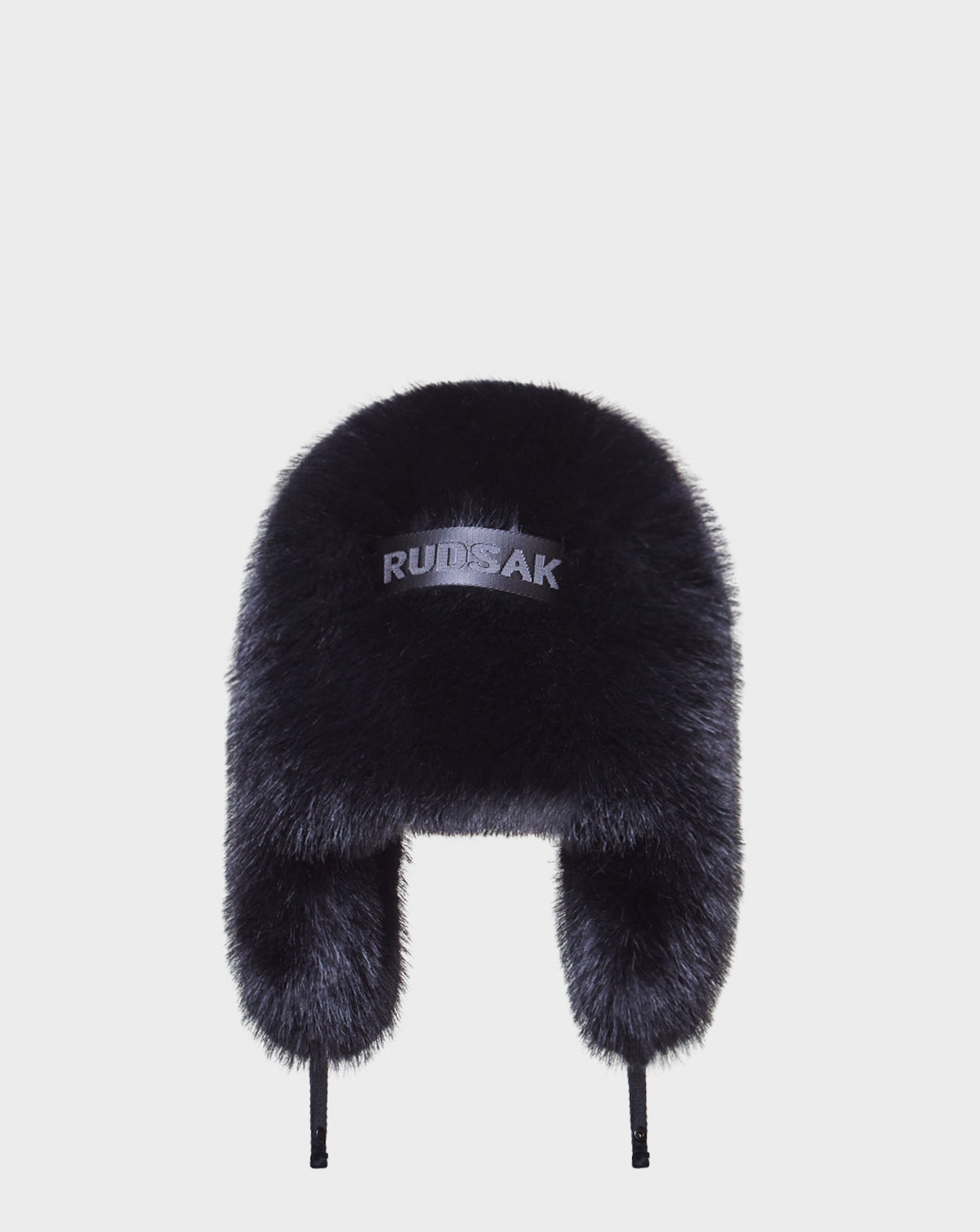 The DARBY - 9422510 BLACK is a black unisex aviator hat with ear flaps, made from faux fur, featuring "Rudsak" embroidered on the front and displayed against a plain white background.