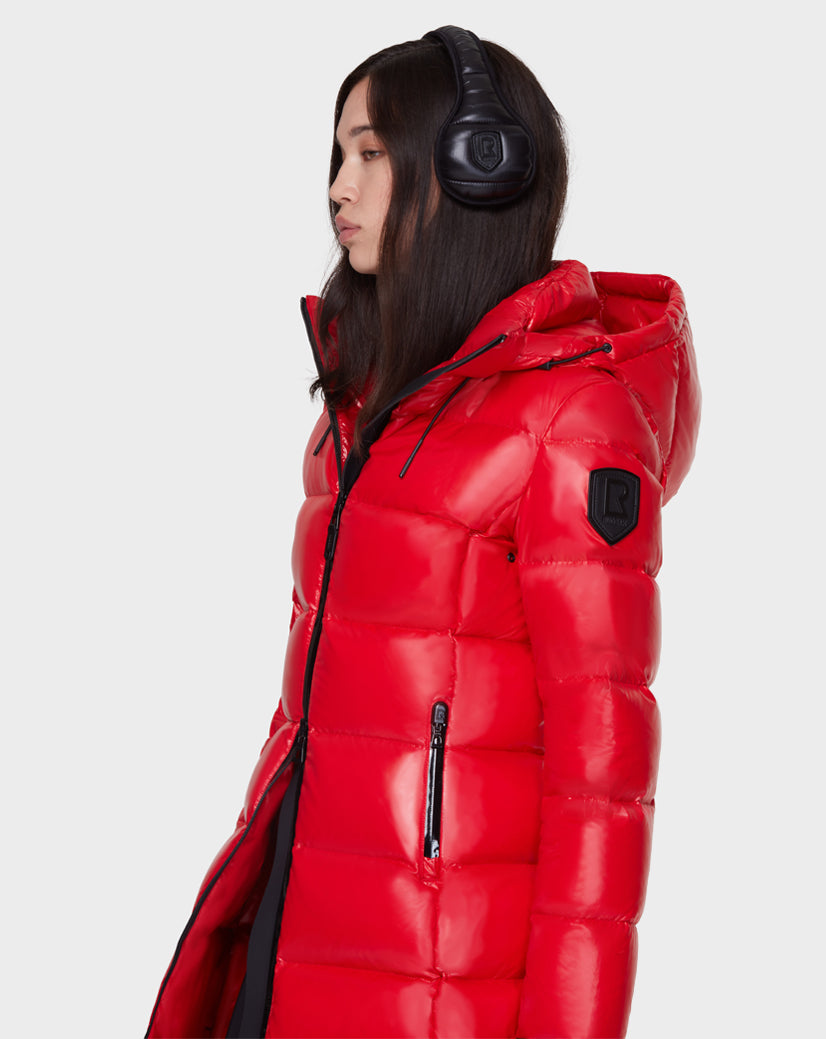 A woman with long dark hair wears black headphones and the Rudsak IRENE - CA EN 8421513 BLACK puffer jacket, standing against a light background and highlighting this stylish cold-weather piece.