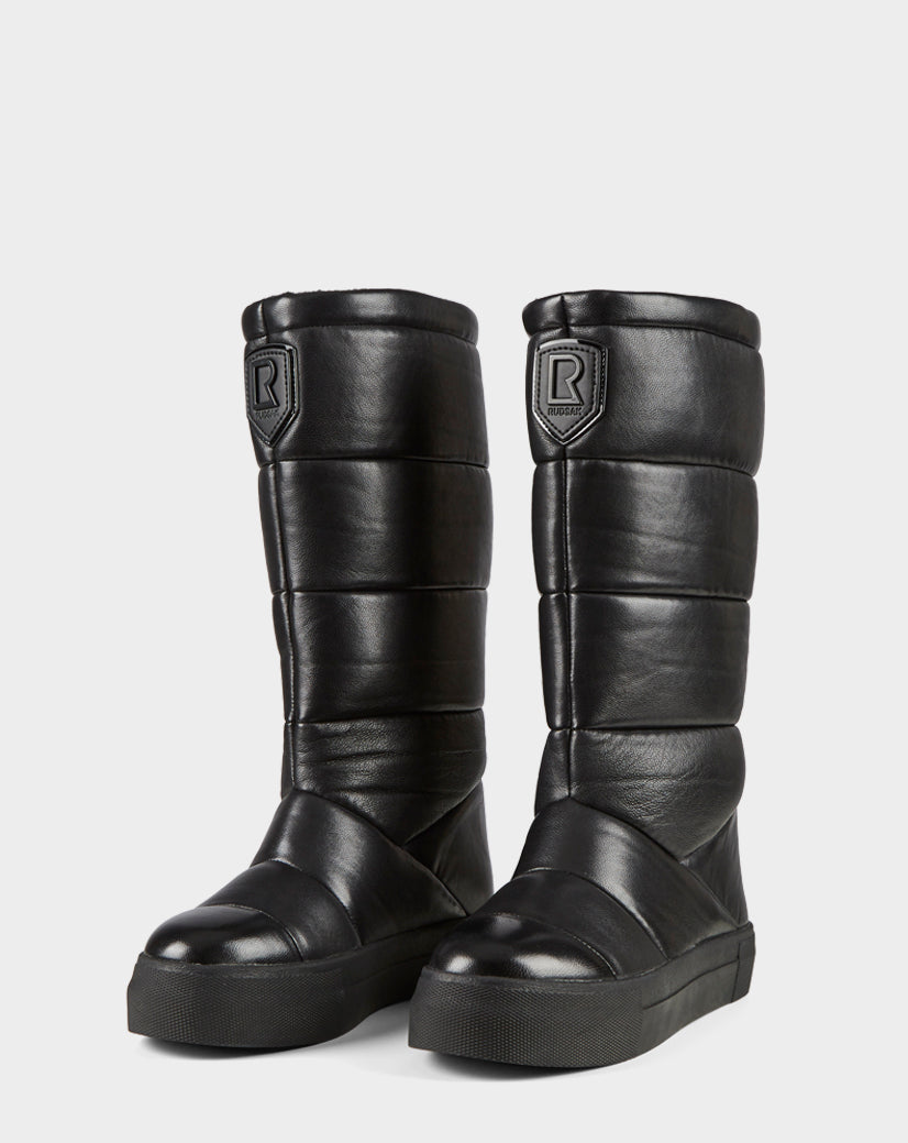 The TEIGEN - CA EN 8220533 BLACK by Rudsak are tall, black, quilted leather knee-high boots with thick soles and an “R” patch near the top. Their shiny, padded look delivers urban winter style.