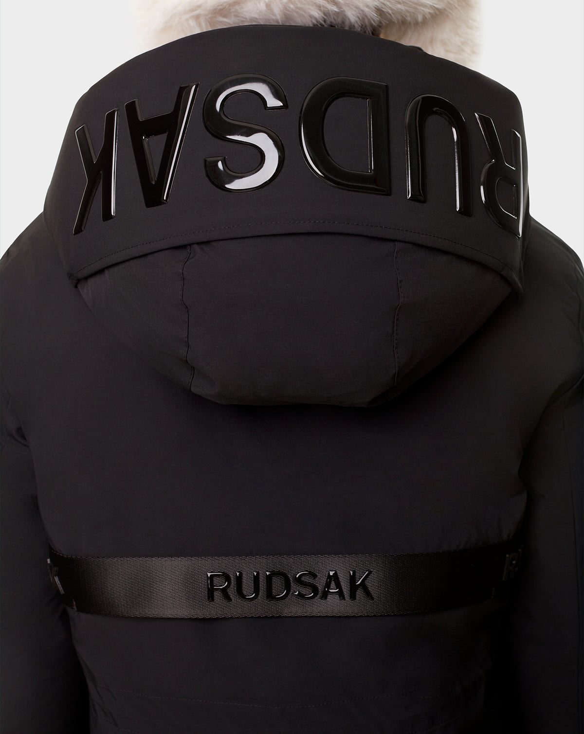 Back view of the RUDSAK CARLY - 8122514 BLACK down jacket featuring a fur-trimmed hood, shiny black RUDSAK lettering across the hood and upper back, plus waterproof zippers for sleek, functional winter style.