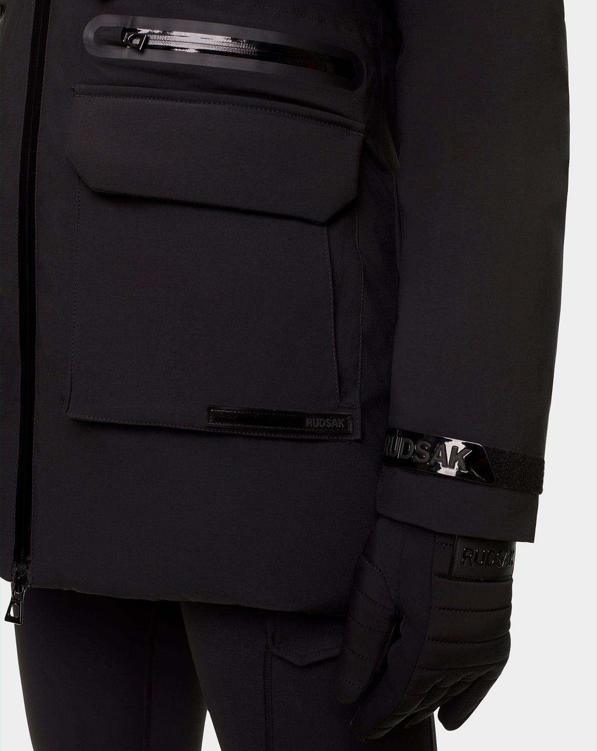 Close-up of a person wearing the RUDSAK CARLY - 8122514 BLACK winter down jacket with large front pockets, black gloves, black RUDSAK logo lettering, and waterproof zippers for added protection.