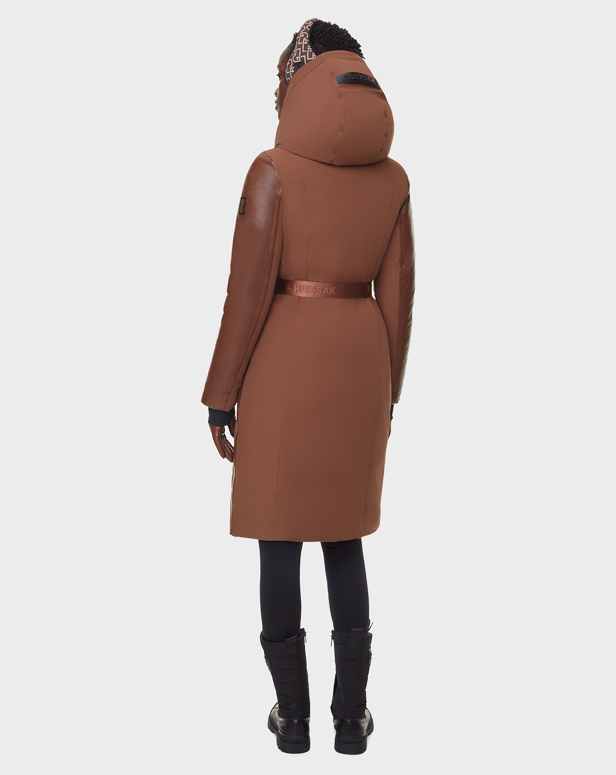 A person wearing the RUDSAK JANIS - 8122571 COHIBA long down parka with black leggings and boots is standing with their back to the camera against a plain white background.
