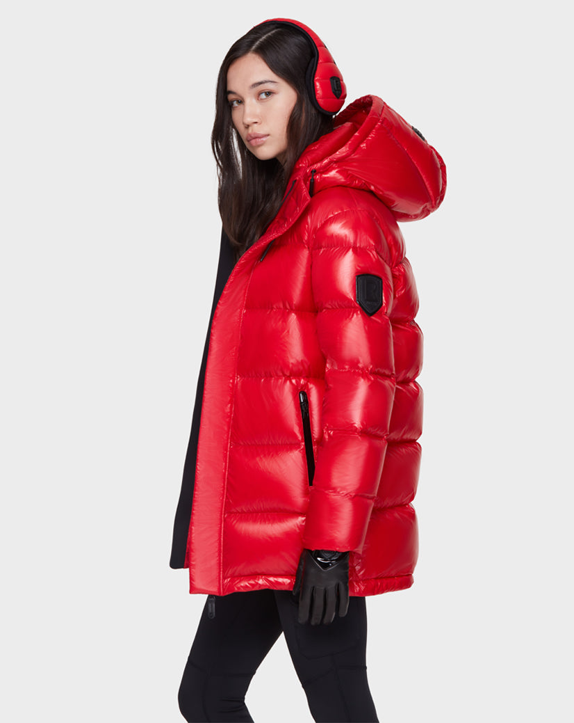 A woman models the Rudsak JOJO - 8121521 POPPY RED down puffer jacket, paired with black gloves and red earmuffs, against a plain light background as she looks over her shoulder at the camera.