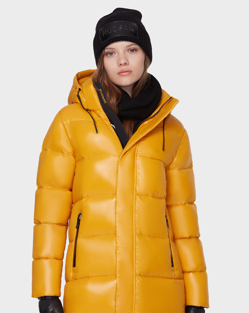 A woman wearing the Rudsak MAO - 8121506 YELLOW puffer coat, paired with a black knit beanie, scarf, and gloves, stands against a plain white background.