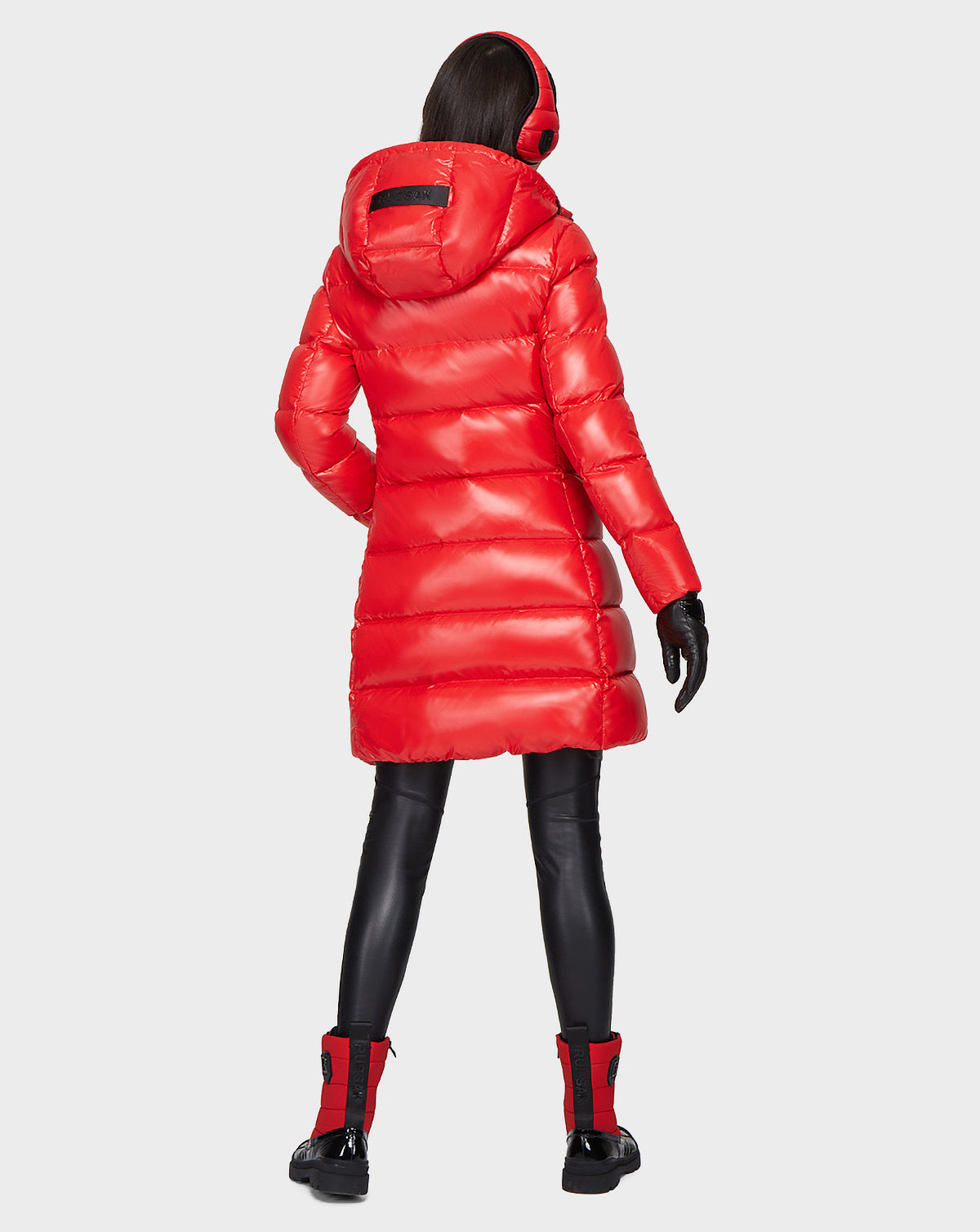 A person in the Rudsak MILIA - 8121552 POPPY RED women’s down puffer with a hood stands facing away, paired with black leggings, red and black boots, black gloves, and red earmuffs against a plain white background.