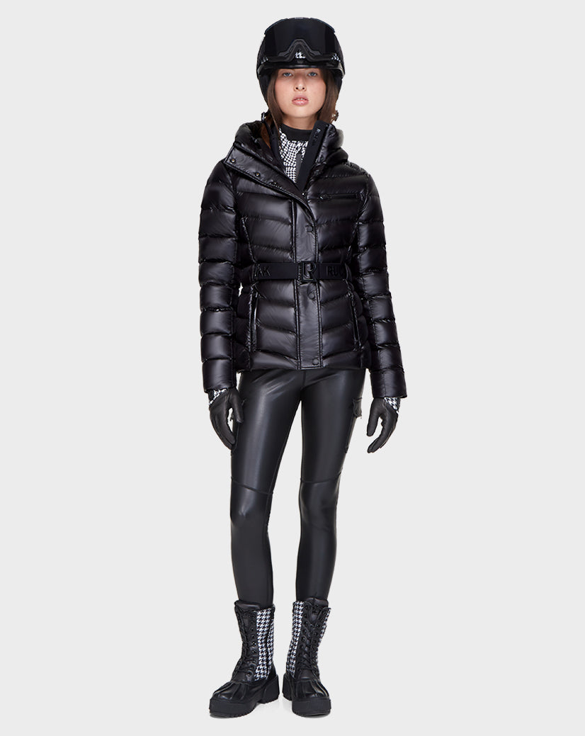 A person wearing the Rudsak MASORA - 8121535 BLACK belted puffer jacket, black helmet, gloves, faux leather pants, and lace-up boots stands against a plain light gray background.
